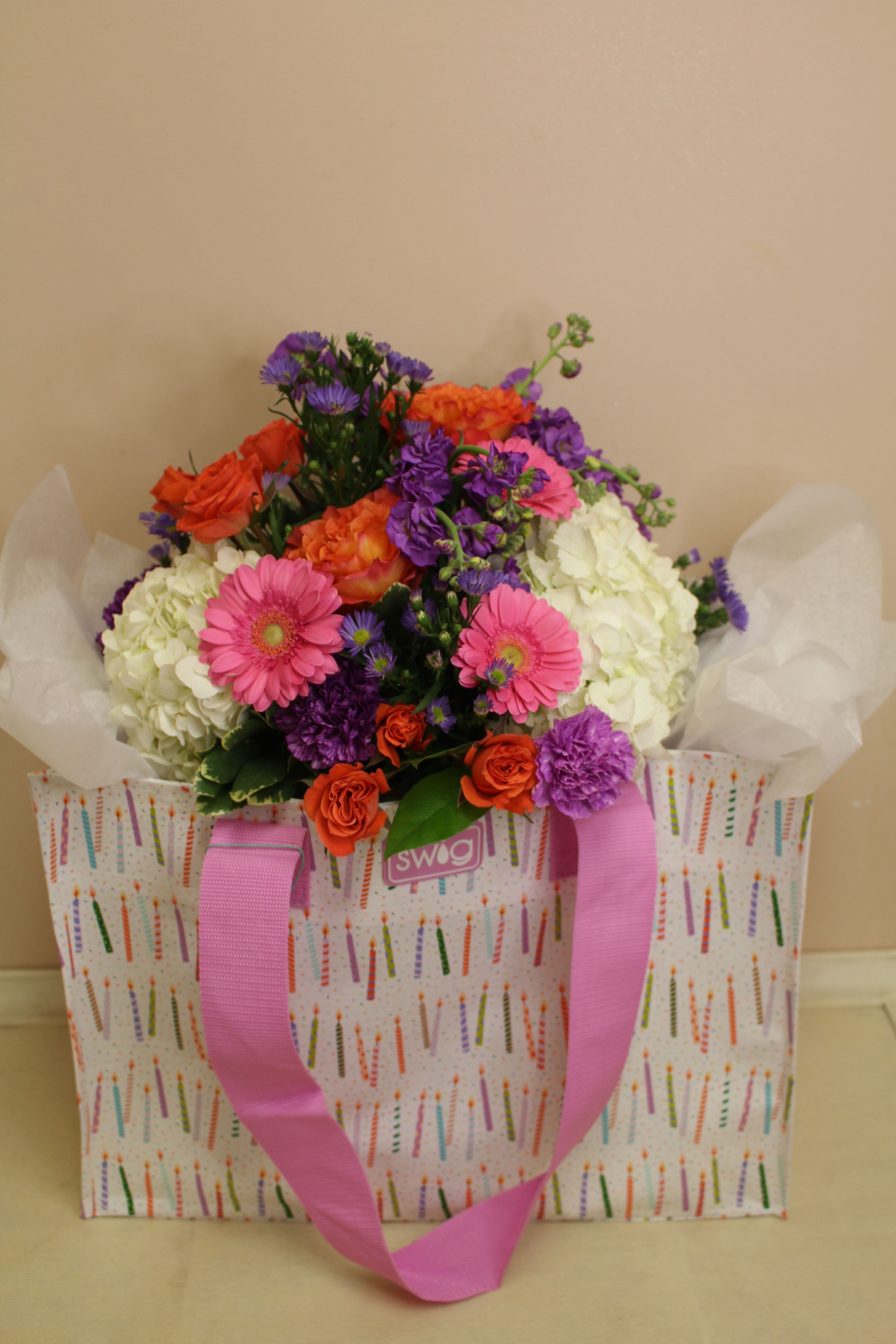 Colorful bouquet in a patterned gift bag with pink ribbon