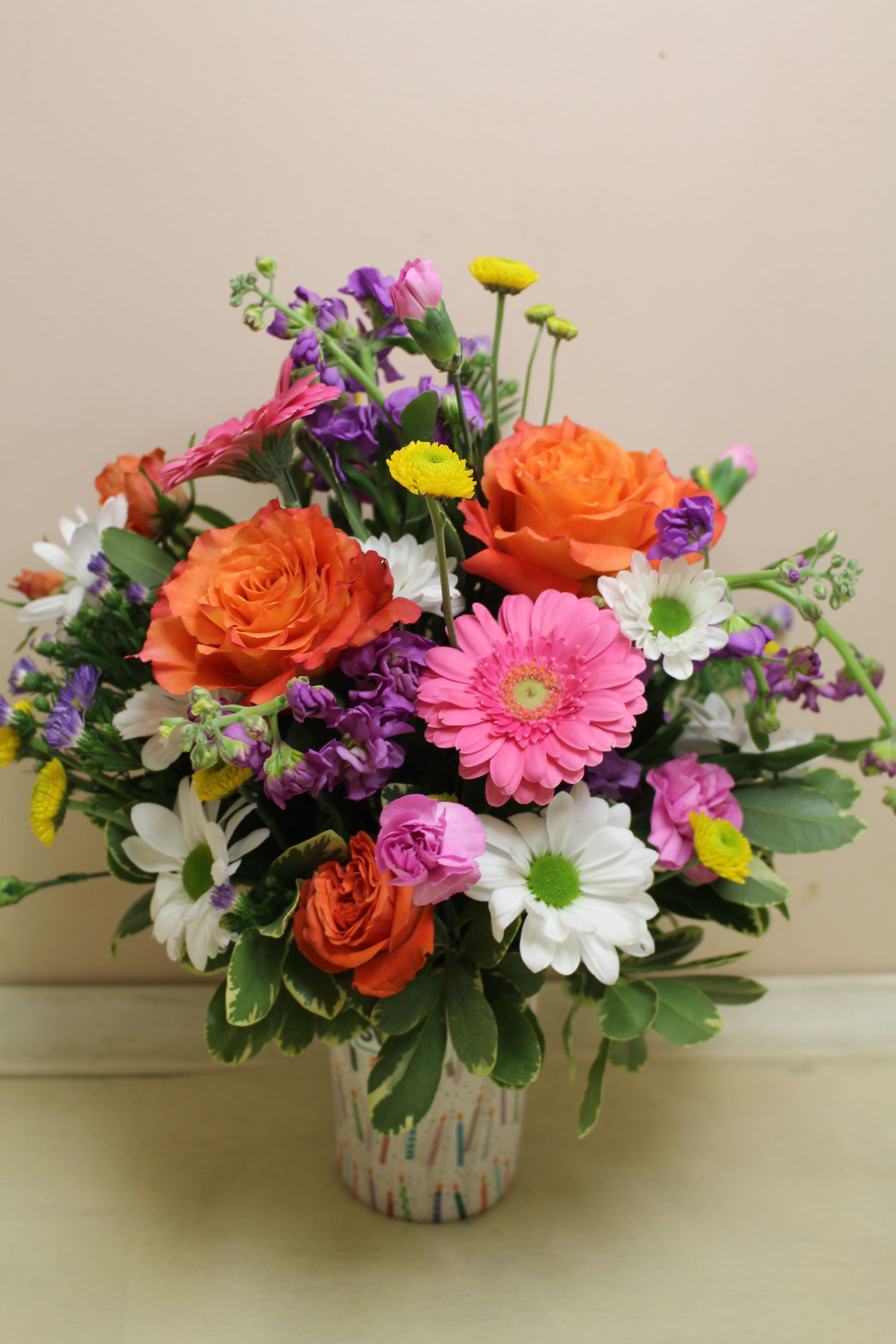 Mixed bouquet of orange roses, pink gerbera daisies, and white daisies in a patterned vase