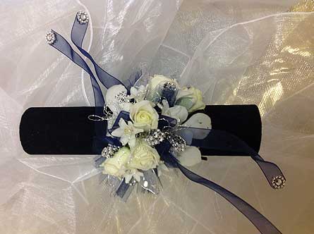 White floral wrist corsage with blue ribbon on a black band
