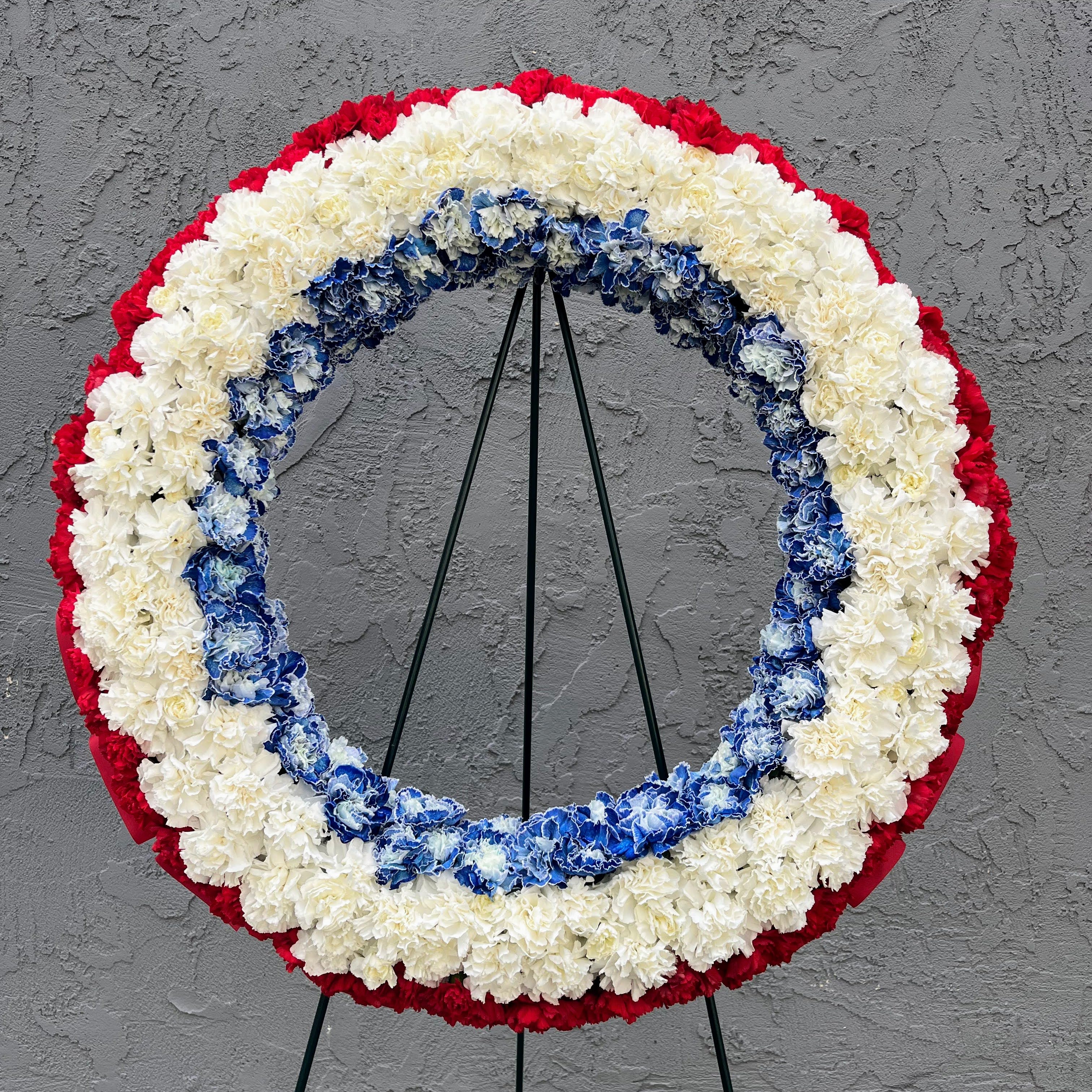 Red, White and Blue Wreath - A standing wreath that can be sent as a gift of condolence. Our Red, White and Blue Wreath features red, white and blue carnations, it measures 24" and comes with an easel.  We can also add custom-printed ribbons - contact us to order. 