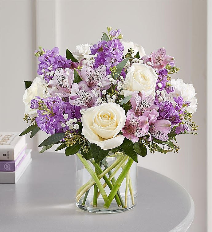 Bouquet of white roses and purple flowers in a clear glass vase