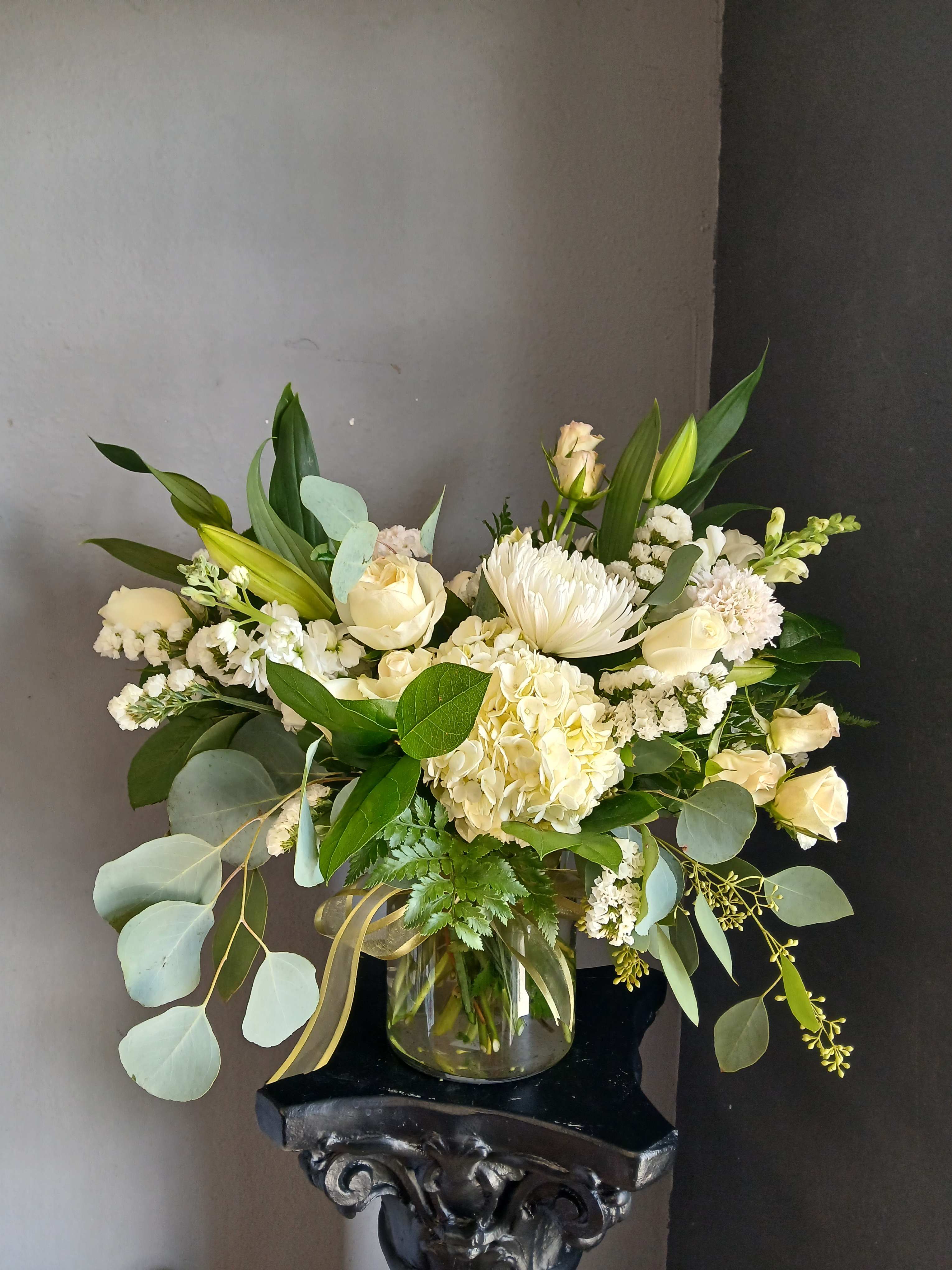 White floral arrangement in a clear glass vase with mixed greenery