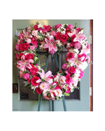 Heart-shaped floral wreath with pink lilies and roses on an easel
