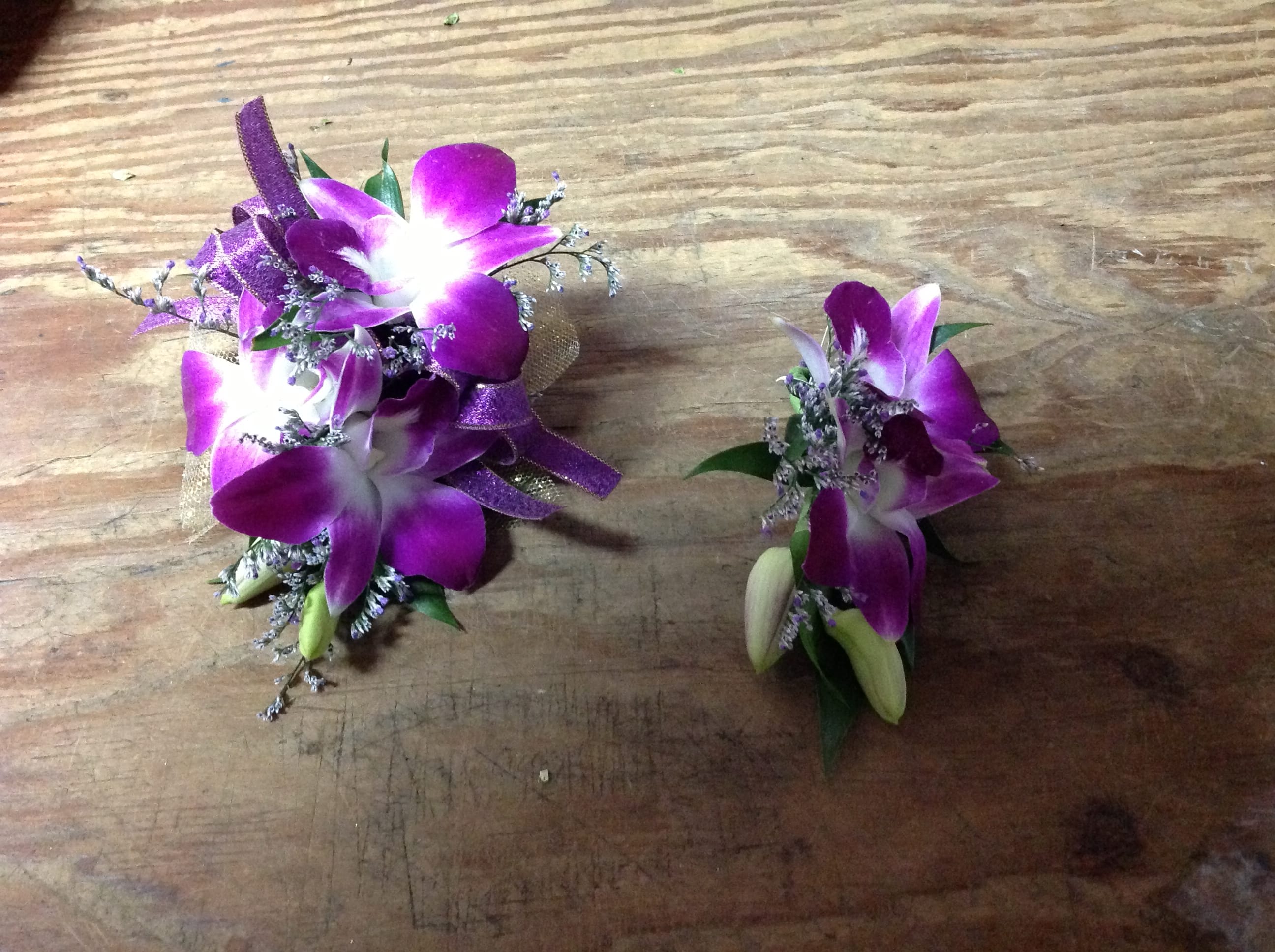 Two purple orchid corsages with ribbon accents on a wooden surface