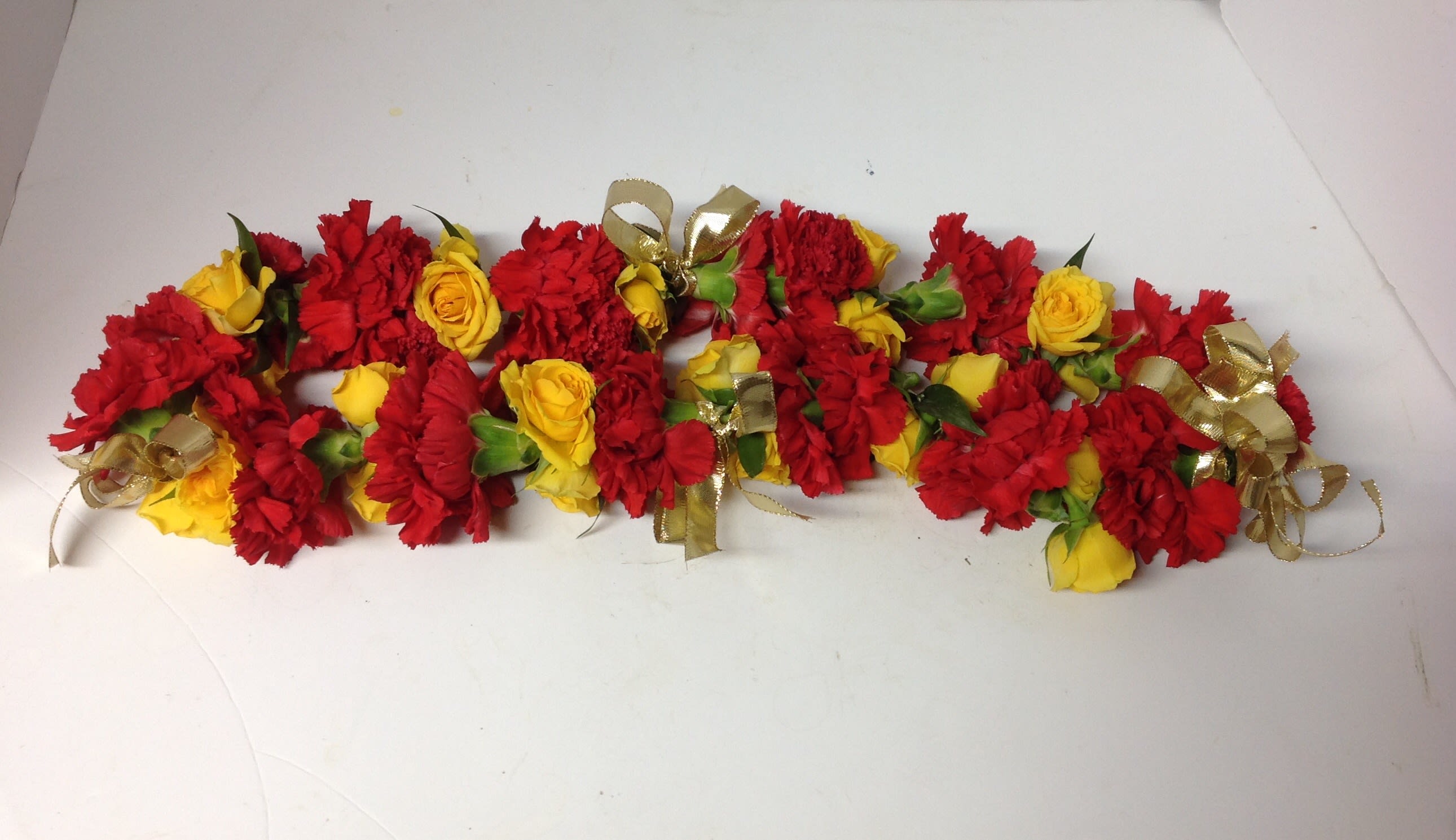 Red and yellow flower garlands with gold ribbon bows on a white surface