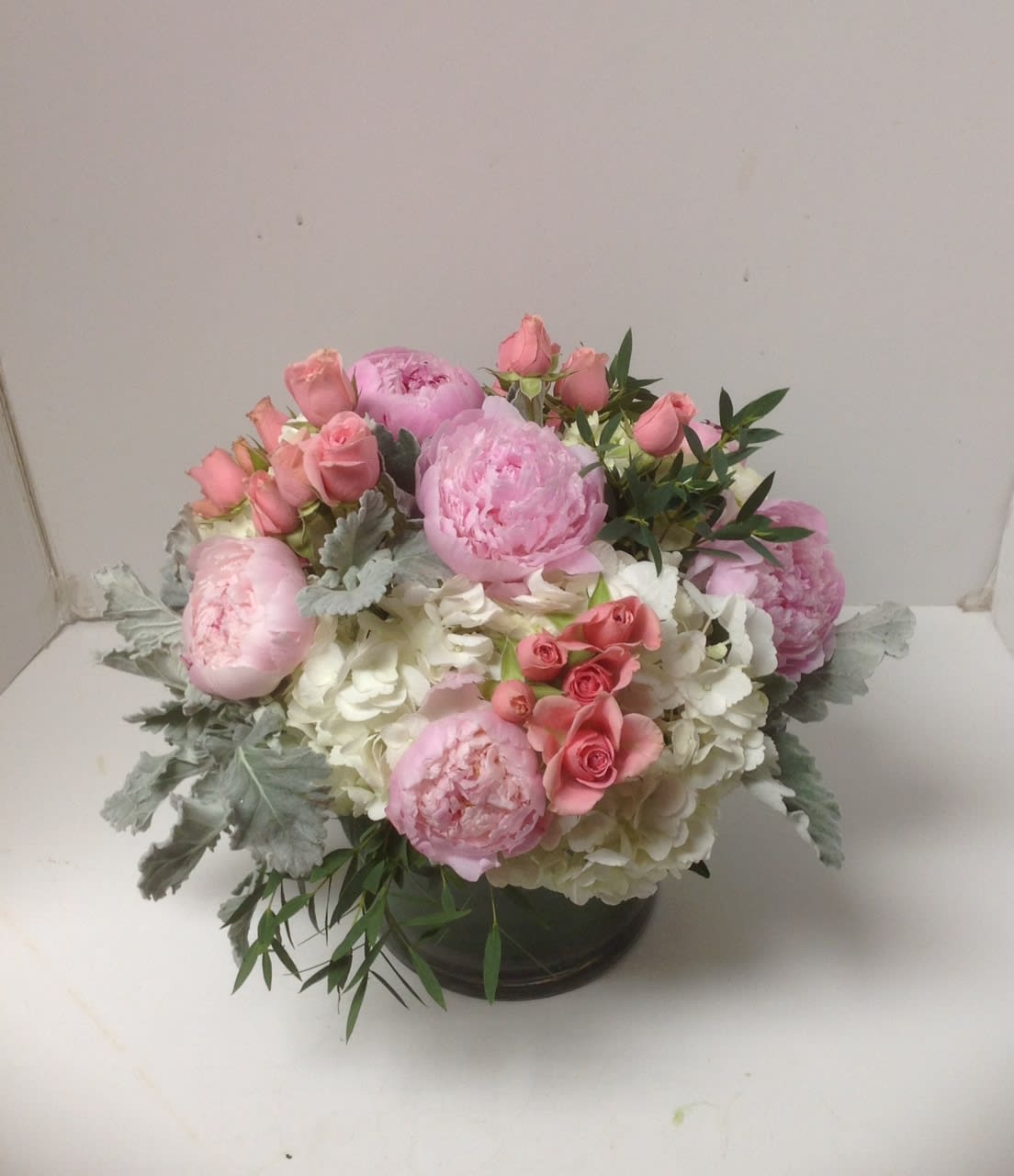 Low arrangement of pink peonies and roses with white hydrangeas in a clear glass vase