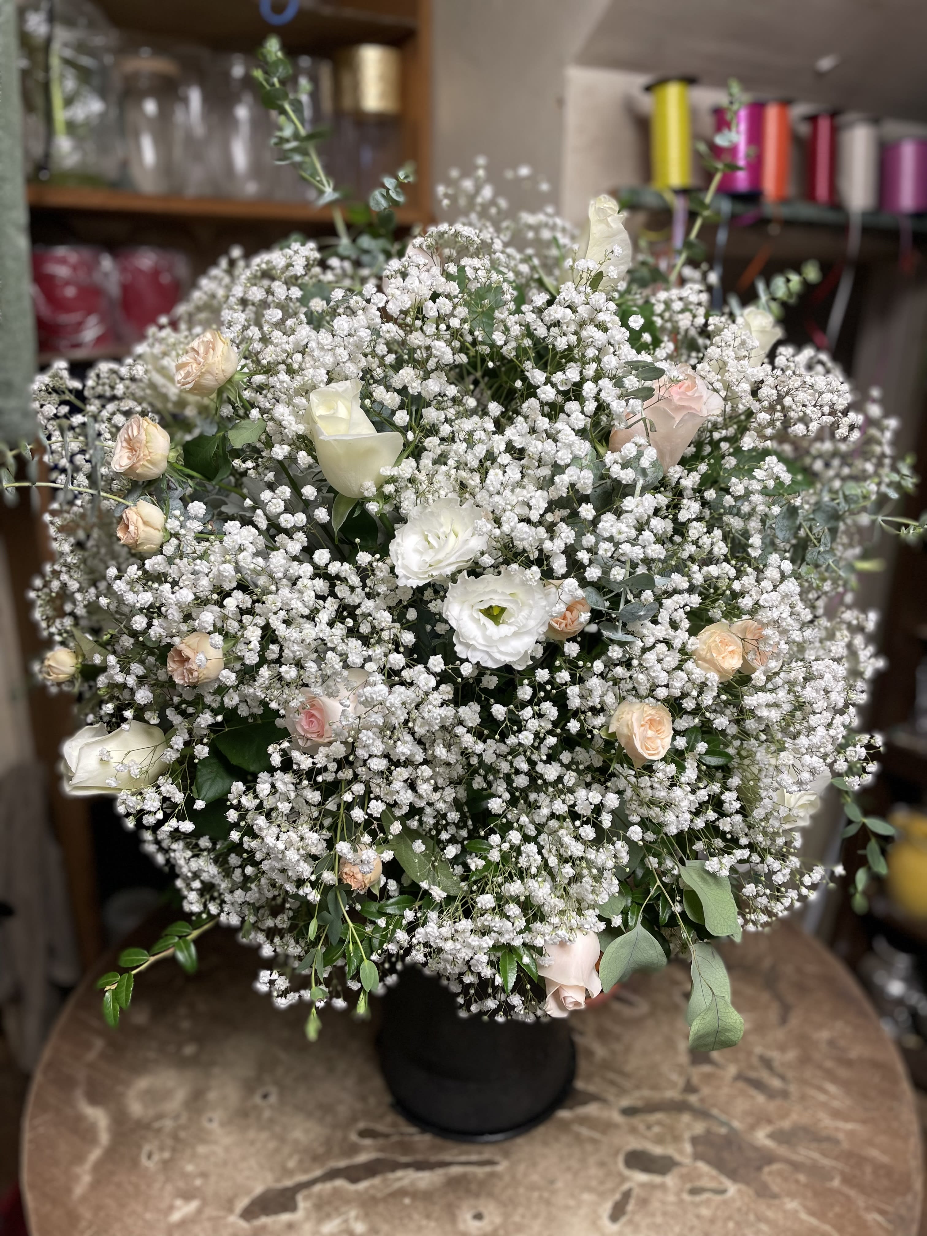Large white floral arrangement with small pink roses in a black vase