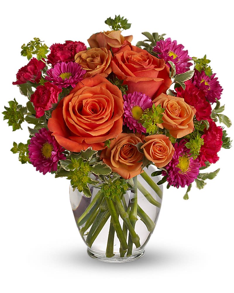 Compact arrangement of orange roses with bright pink mums and carnations in a clear glass vase