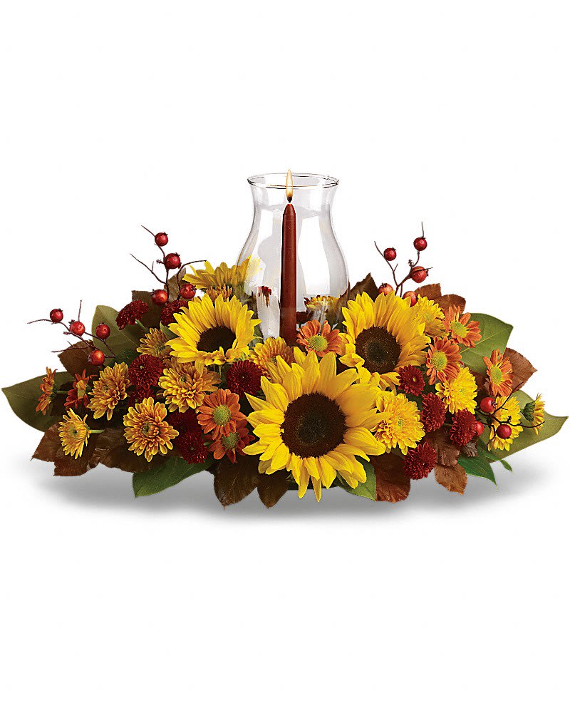Sunflower Centerpiece - Symbolizing warmth and happiness, it is no wonder the sunflower is a quintessential ingredient in so many fall bouquets. This centerpiece maximizes the joy of sunflowers by arranging them with a bevy of fall flowers, foliage and a cranberry hued candle under hurricane glass. Along with brilliant sunflowers, you'll find yellow spray roses, bronze and rust chrysanthemums, red berries, magnolia leaves and of course an elegant tapered candle inside a hurricane vase.