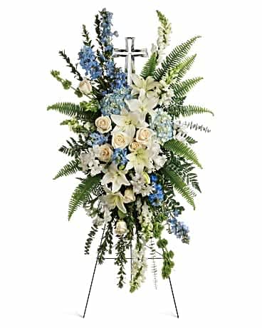 Standing funeral spray with white lilies, blue flowers, and a cross