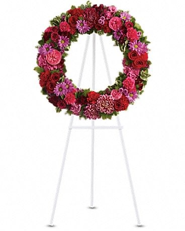 Circular floral wreath on a white easel with red and pink flowers