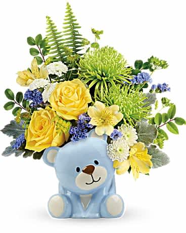 Teleflora's Joyful Blue Bear Bouquet - Welcome the new bundle of love with this sunny yellow rose bouquet, charmingly presented in a sweet ceramic teddy bear. This joyful arrangement features yellow roses, yellow alstroemeria, green spider chrysanthemums, white button spray chrysanthemums, blue sinuata statice, bupleurum, dusty miller, huckleberry, and sword fern. Delivered in a baby blue Bundle of Love Bear.