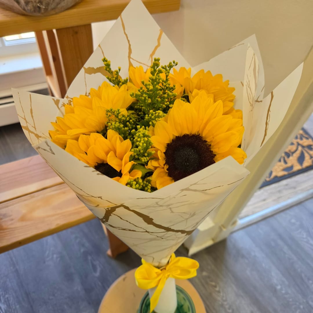 Bouquet of yellow sunflowers wrapped in white paper with a yellow ribbon