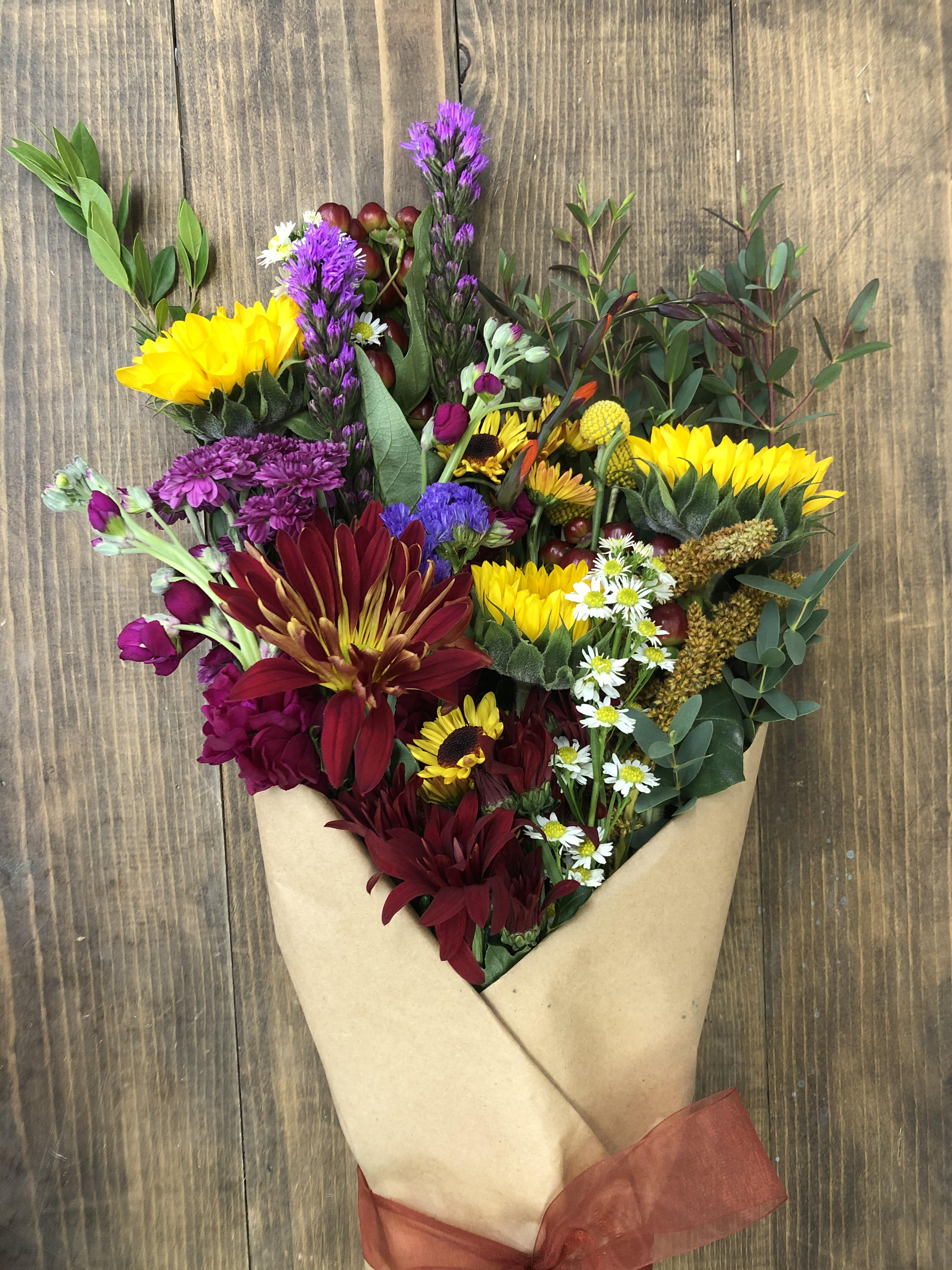 Bouquet of mixed flowers wrapped in brown paper with a red ribbon