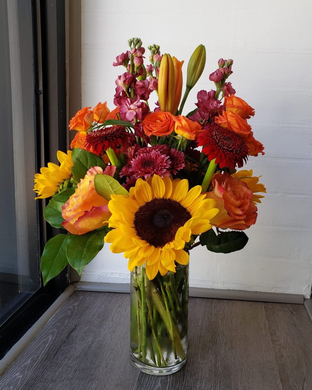 Mixed bouquet of sunflowers, roses, and orange blooms in a glass vase