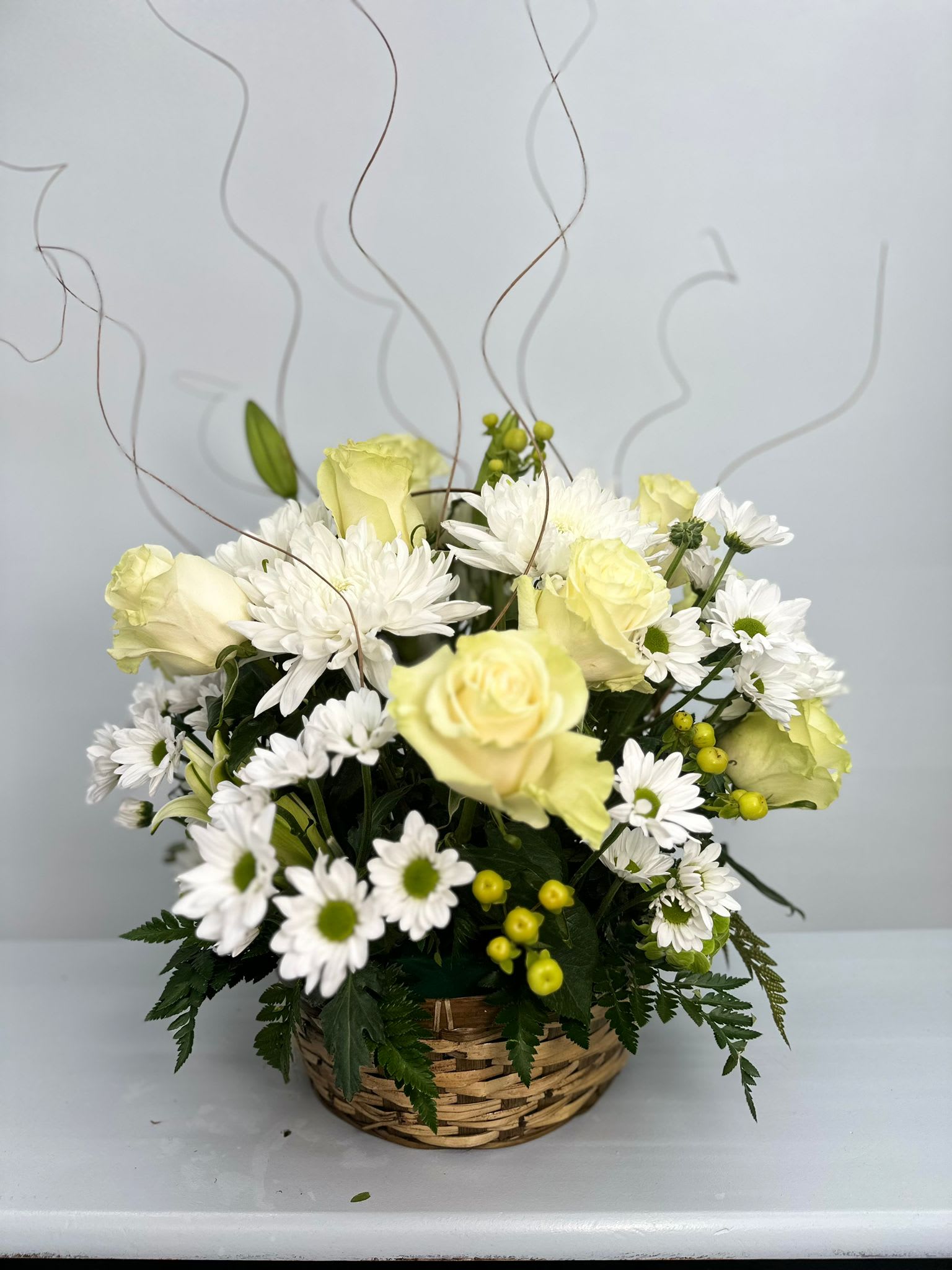 Basket arrangement of pale yellow roses and white daisies