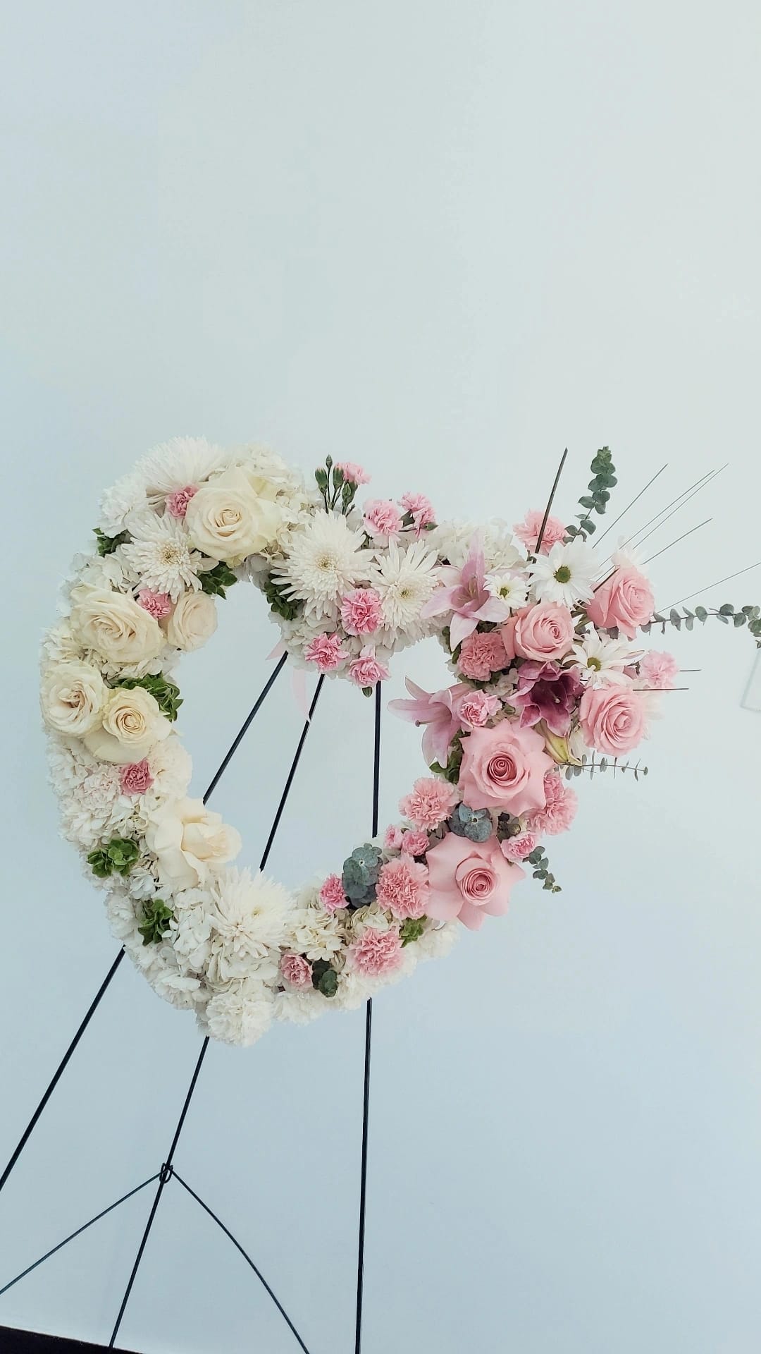 Heart-shaped floral wreath with white and pink flowers on a stand