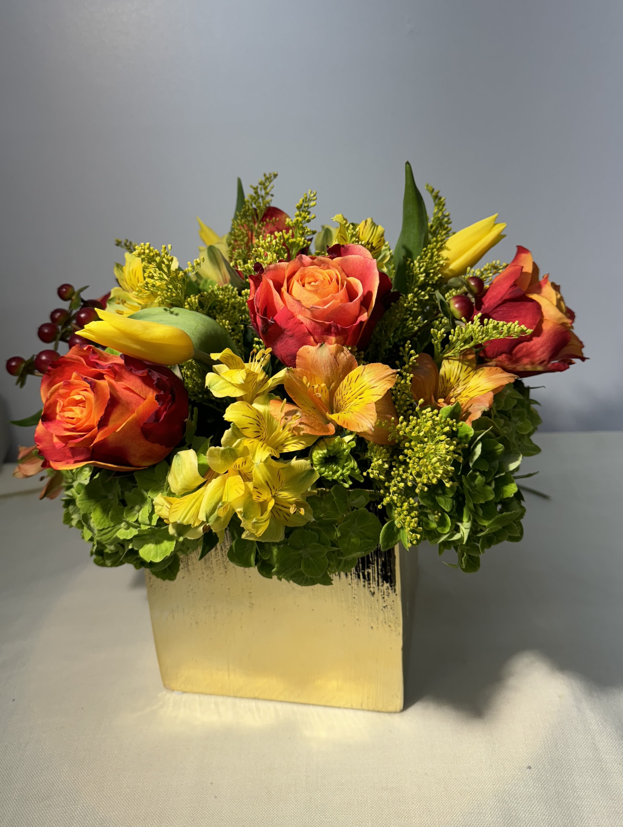 Orange and red roses with yellow flowers in a gold vase