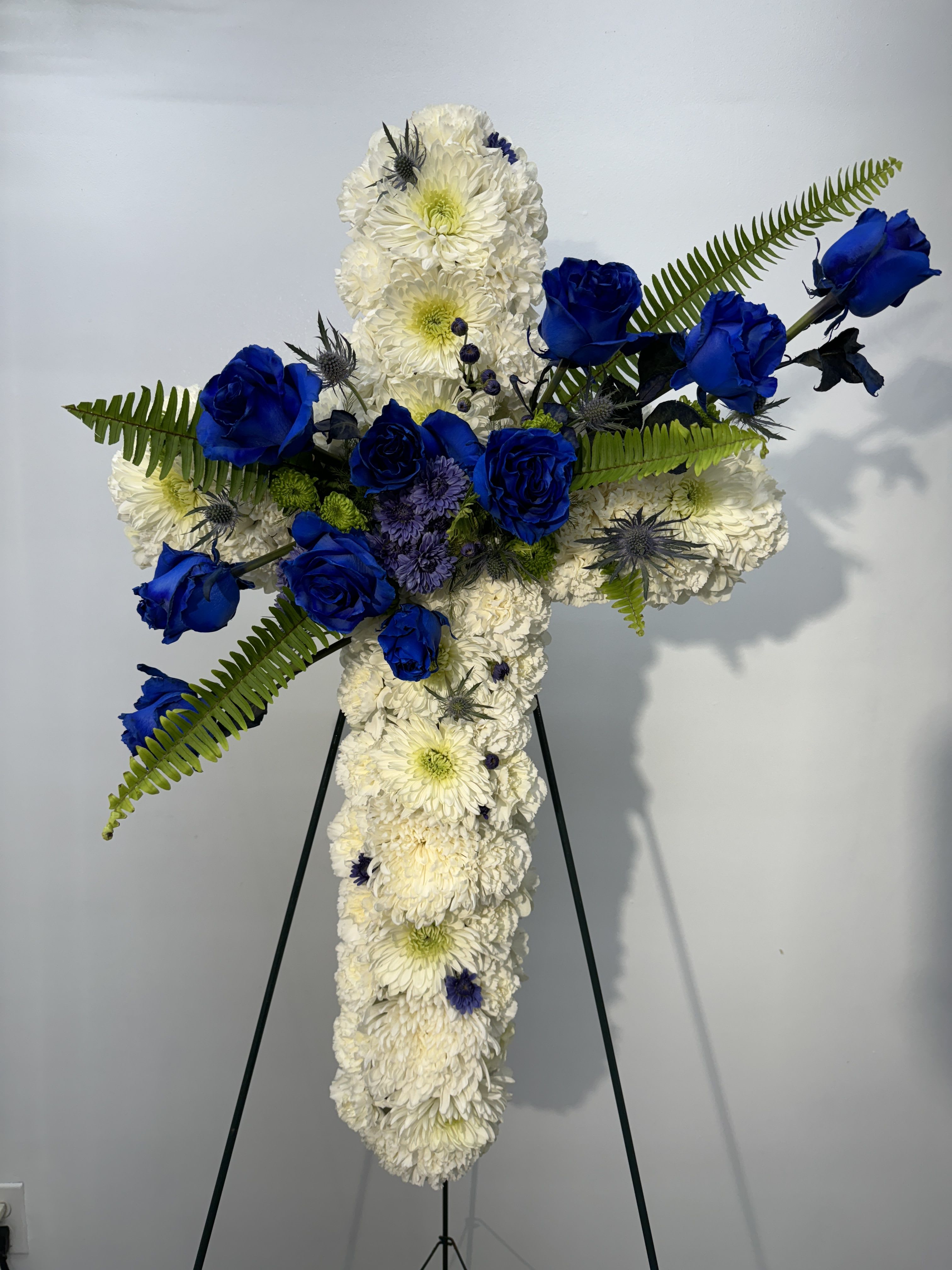 Cross-shaped floral tribute with white chrysanthemums and blue roses on an easel