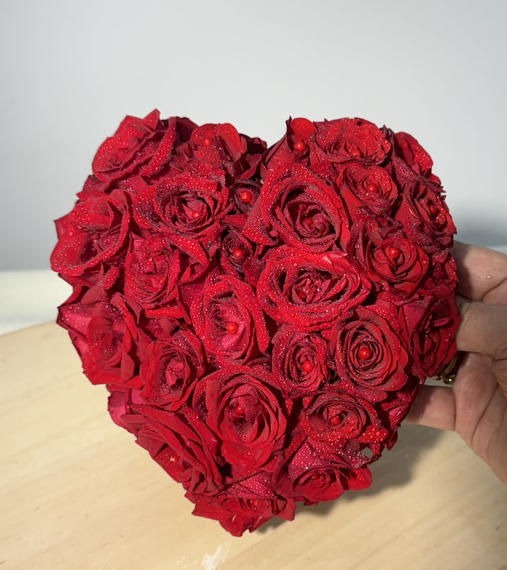 Heart-shaped arrangement of red roses held in a hand