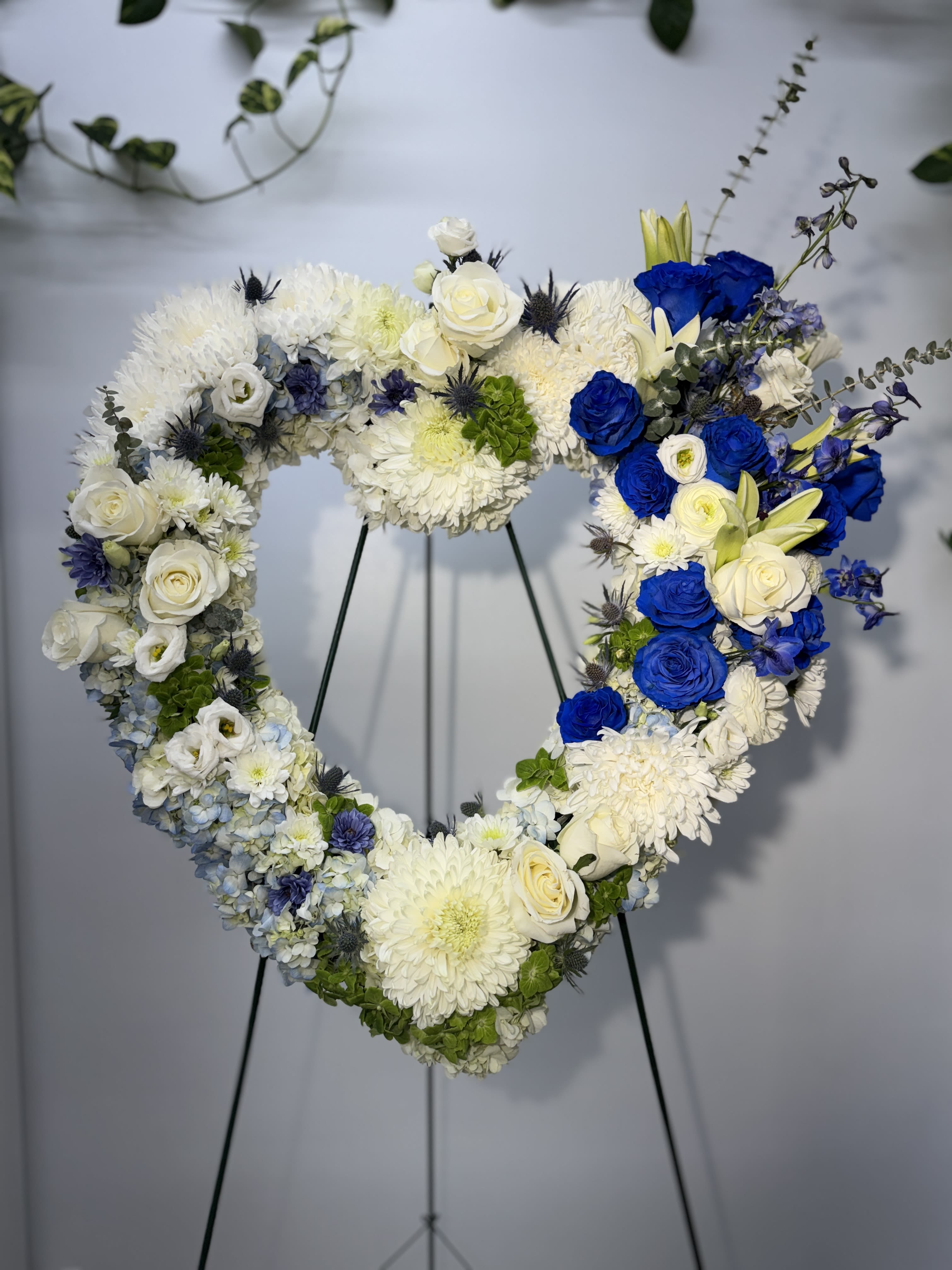 Heart-shaped floral wreath with white and blue flowers on a stand