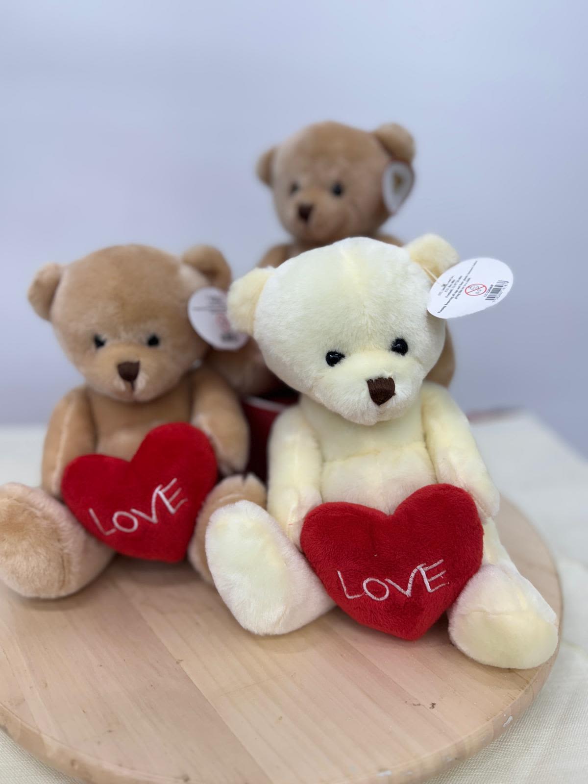 Three teddy bears holding red hearts on a round wooden base