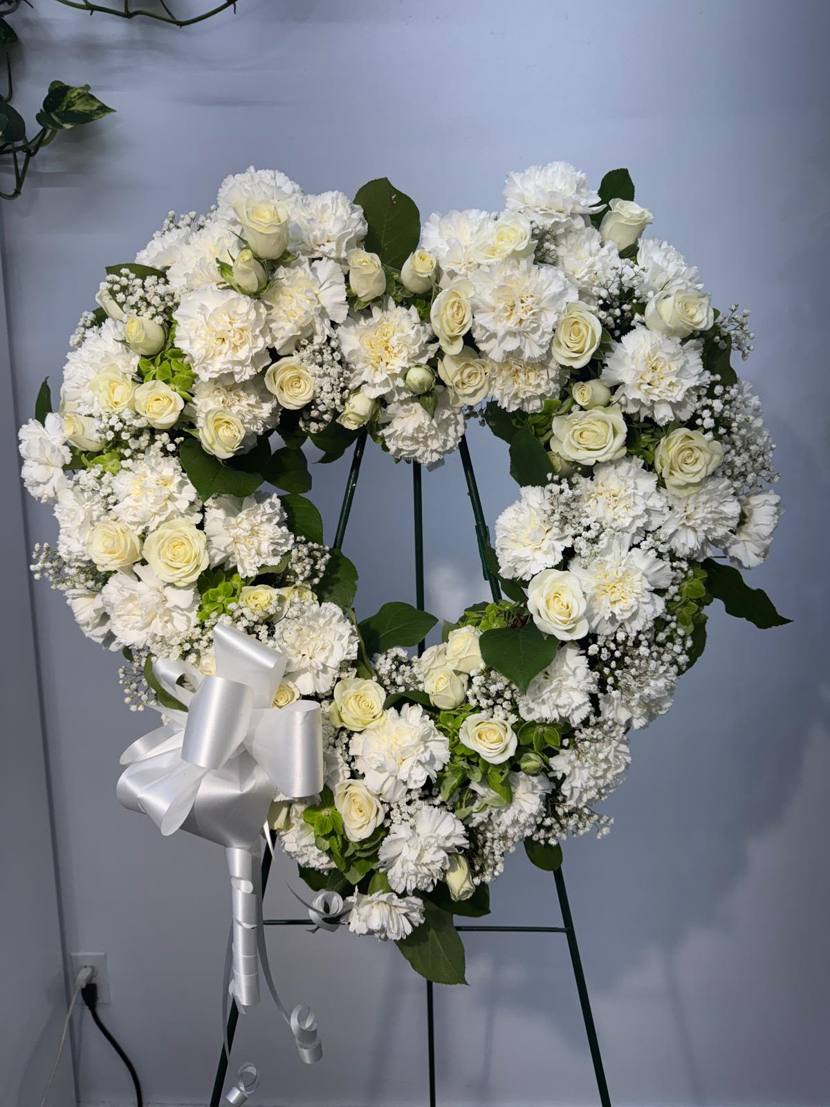 Heart-shaped white floral wreath on an easel with a silver bow