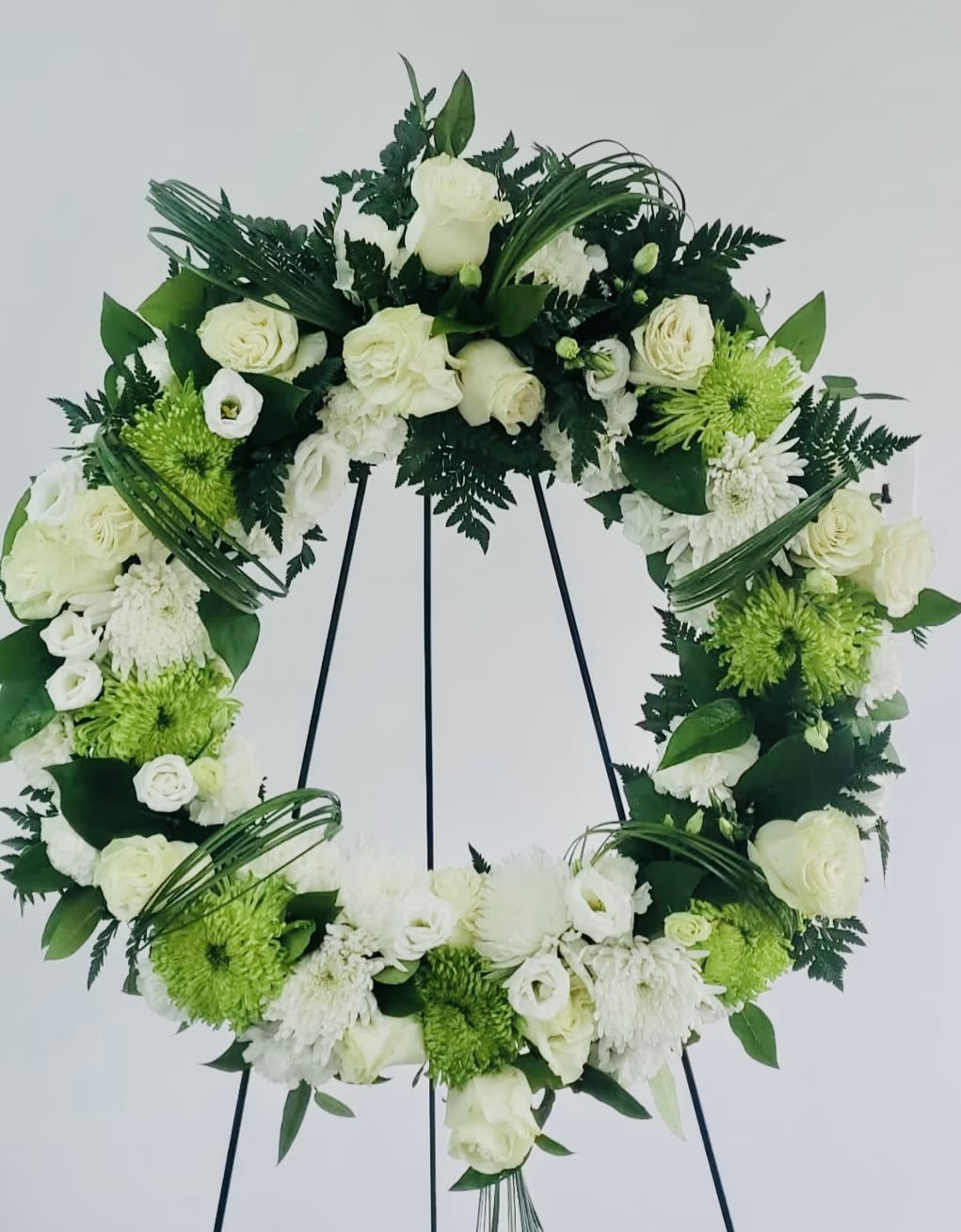 White floral wreath on a black stand with green accents
