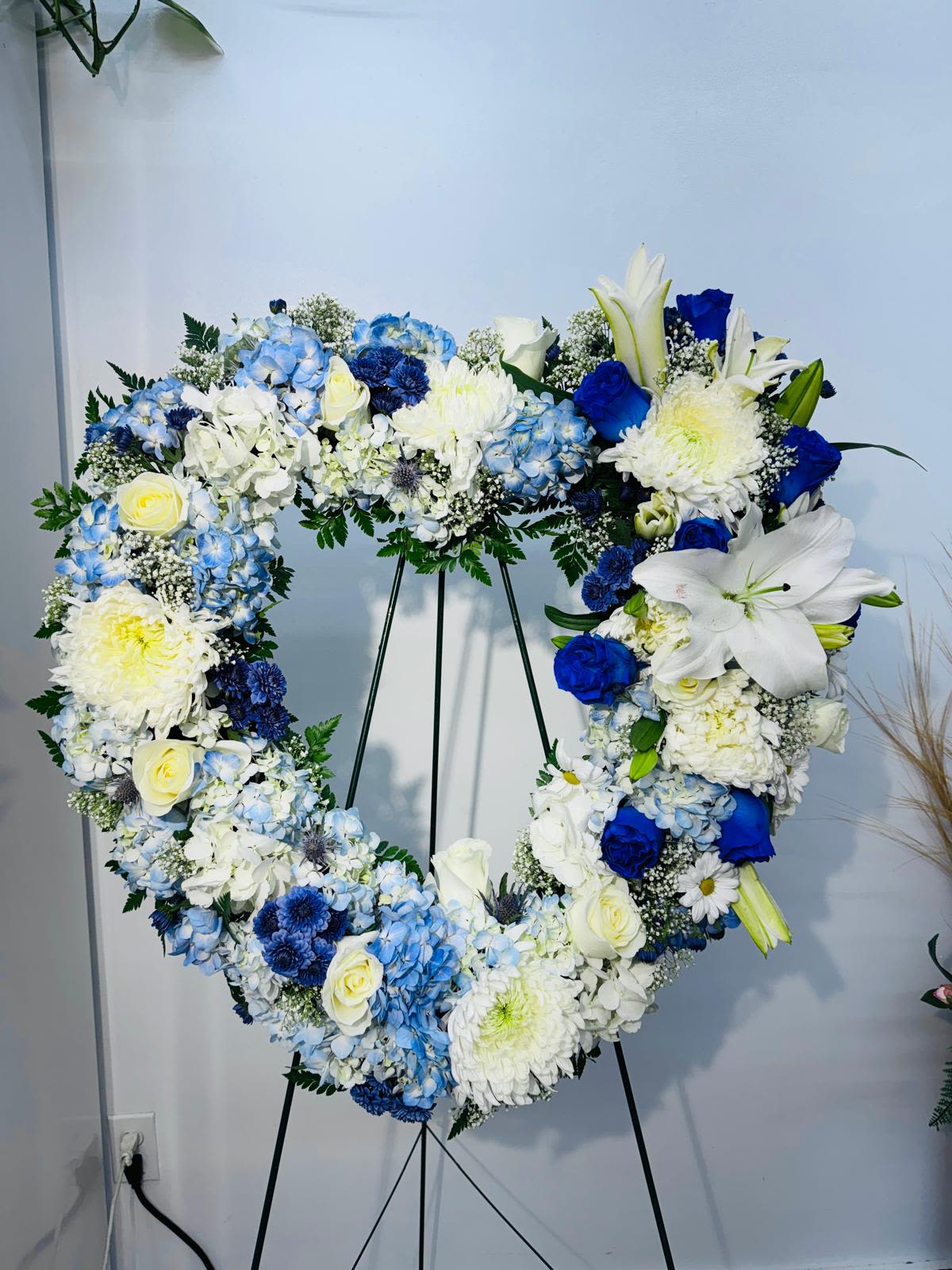 Heart-shaped floral wreath with blue, white, and yellow flowers on a stand