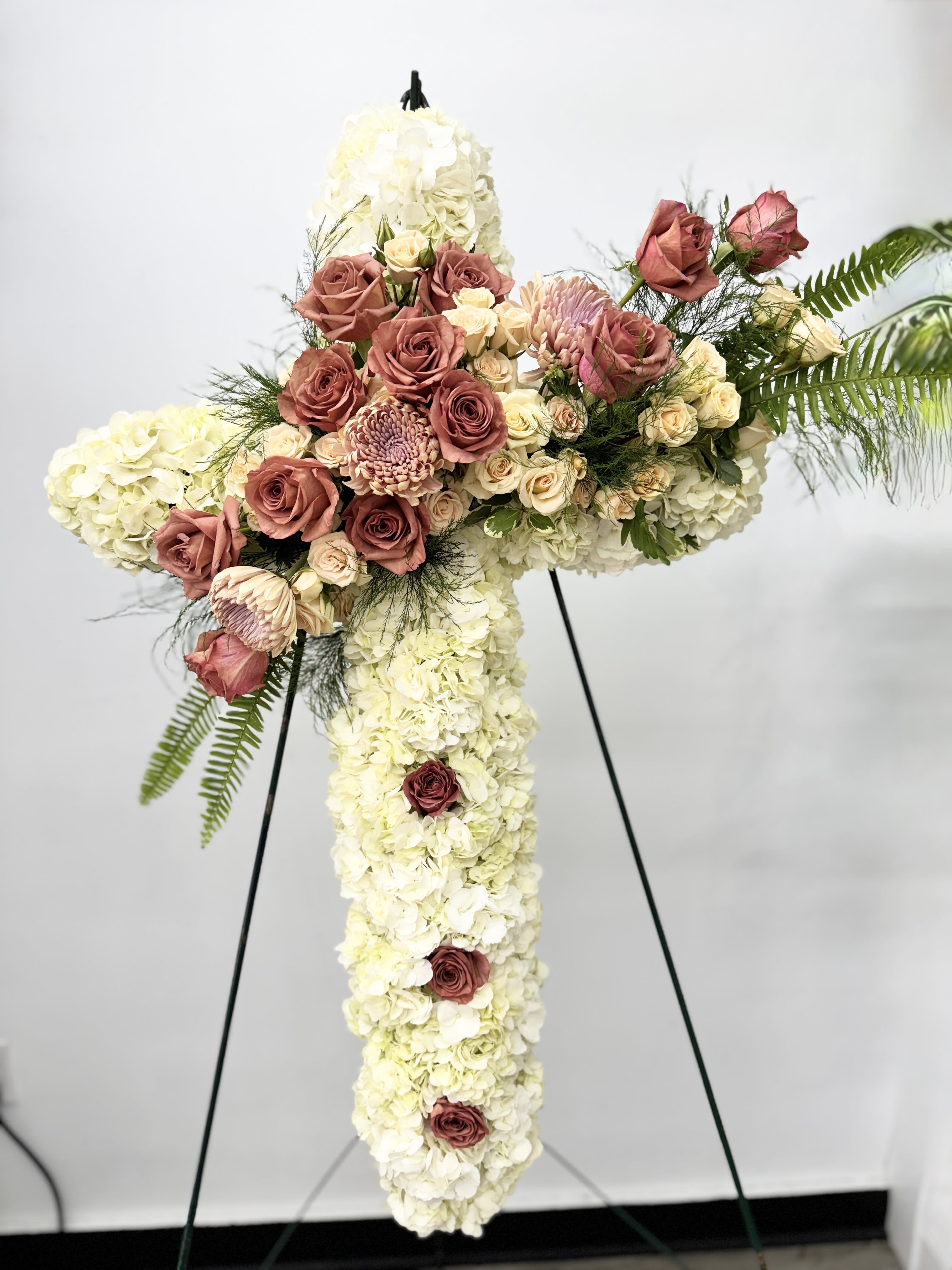 Cross-shaped floral spray with white hydrangeas and pink roses on a stand