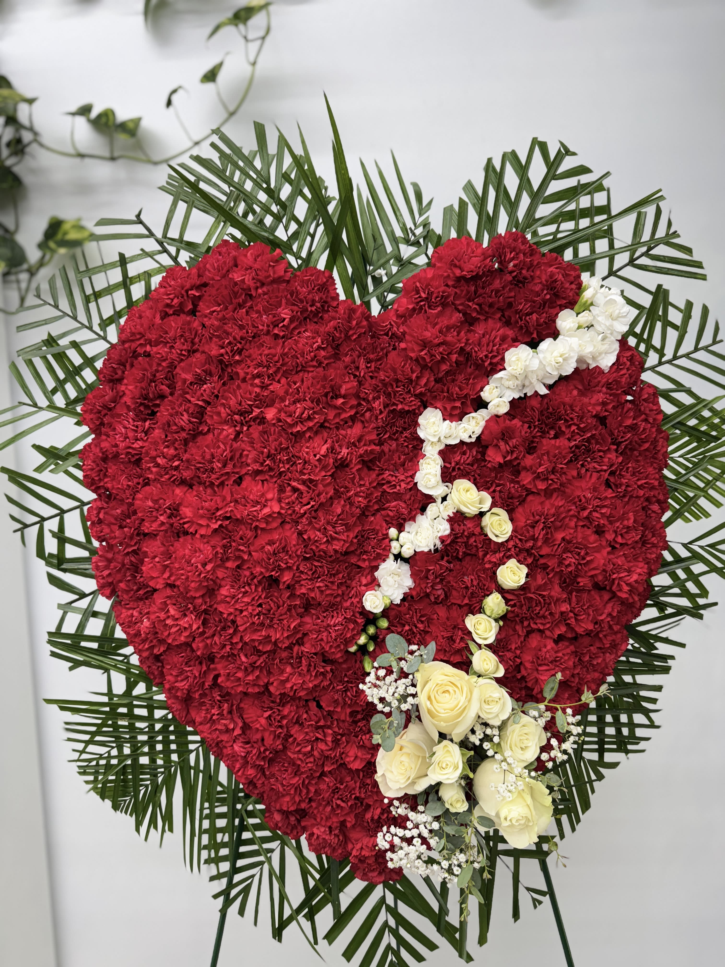 Heart-shaped red floral tribute with white roses and palm fronds