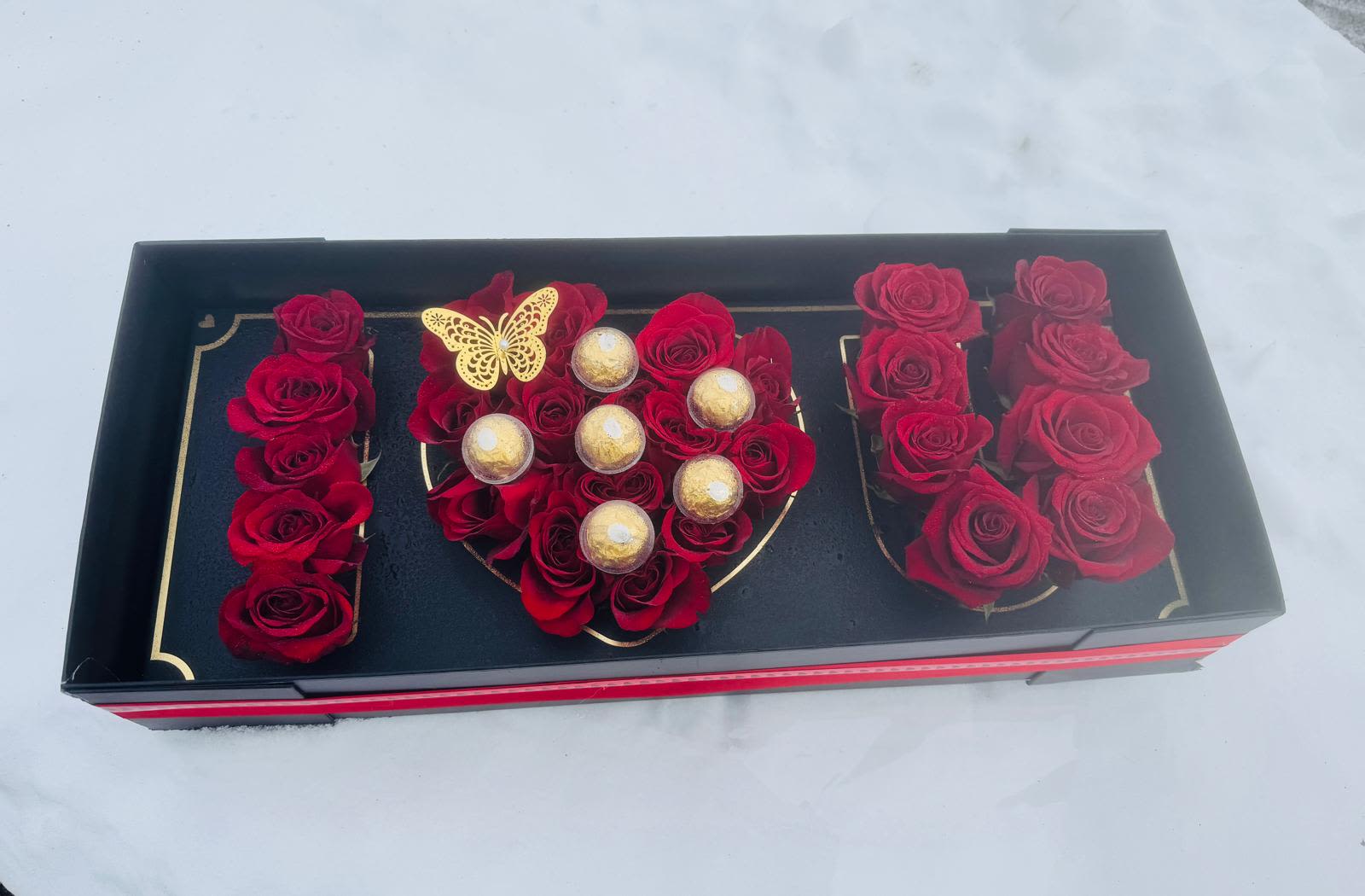 Black gift box with red roses, gold chocolates, and a butterfly decoration