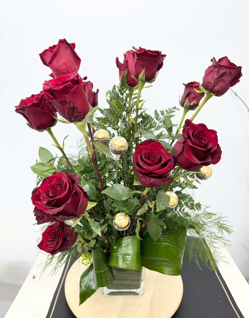 Red roses arranged in a clear square vase with greenery