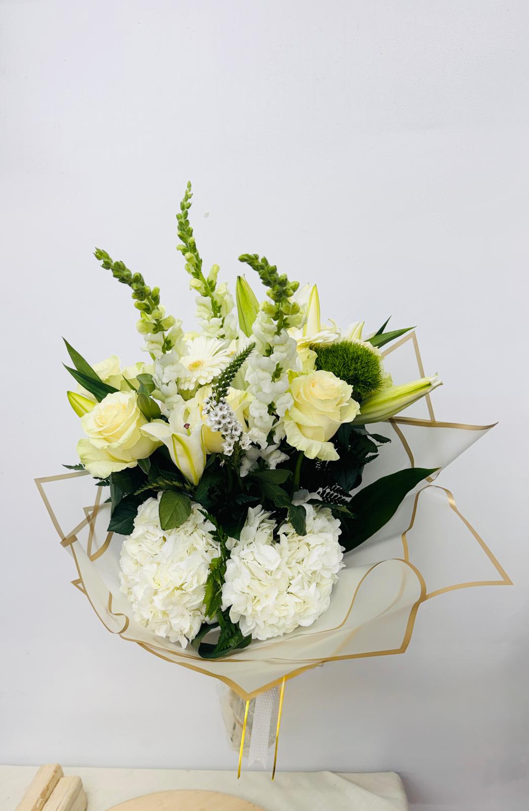Bouquet of white and pale yellow flowers wrapped in clear paper with gold trim