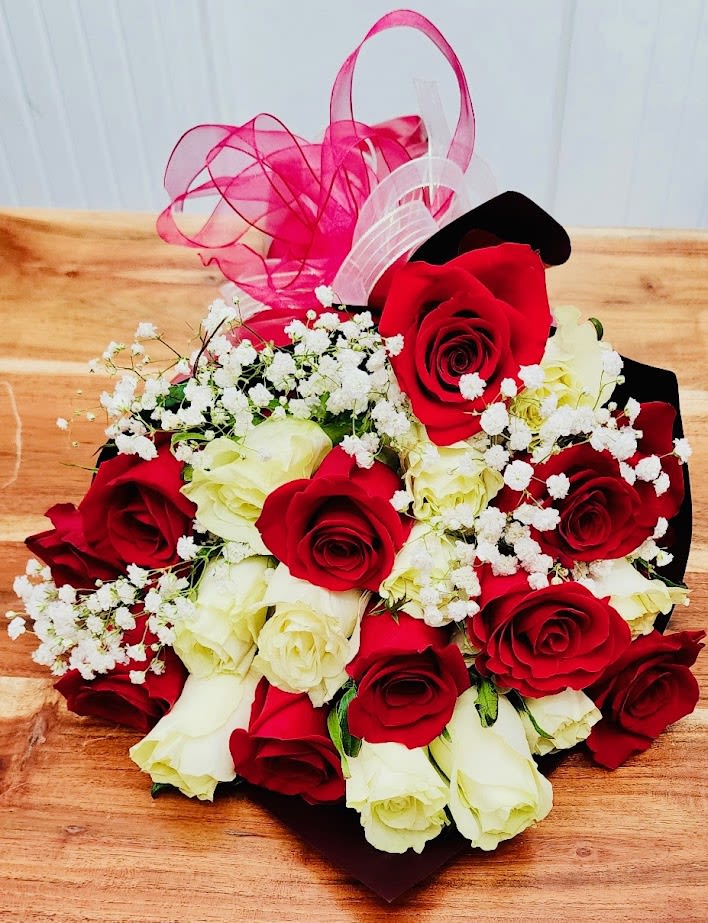 Classic Double Bouquet - A compact bouquet of roses makes an immediate romantic statement - perfect as an anniversary bouquet, Valentine's Day gift, or a "just because" surprise to say I love you. The red and white roses are arranged tightly in a heart formation, with tiny white filler blooms scattered across the surface for a soft, lace-like contrast; loops of sheer pink and white ribbon rise above the arrangement to add a celebratory, gift-ready flourish that will make the recipient feel truly seen.  This wrapped bouquet is presented in a dark decorative paper wrap and tied with both a pink and a white ribbon, giving a polished, classic look that also suits Mother's Day, birthdays, graduations, or get-well wishes. Compact and easy to carry, it contains two dozen roses arranged closely together in the heart shape; the close clustering keeps stems secure and the display looking full for gifting. Ideal year-round - from Easter and spring celebrations through Christmas and winter anniversaries - it's the kind of bouquet that reads as intimate and thoughtful for the person you want to honor.