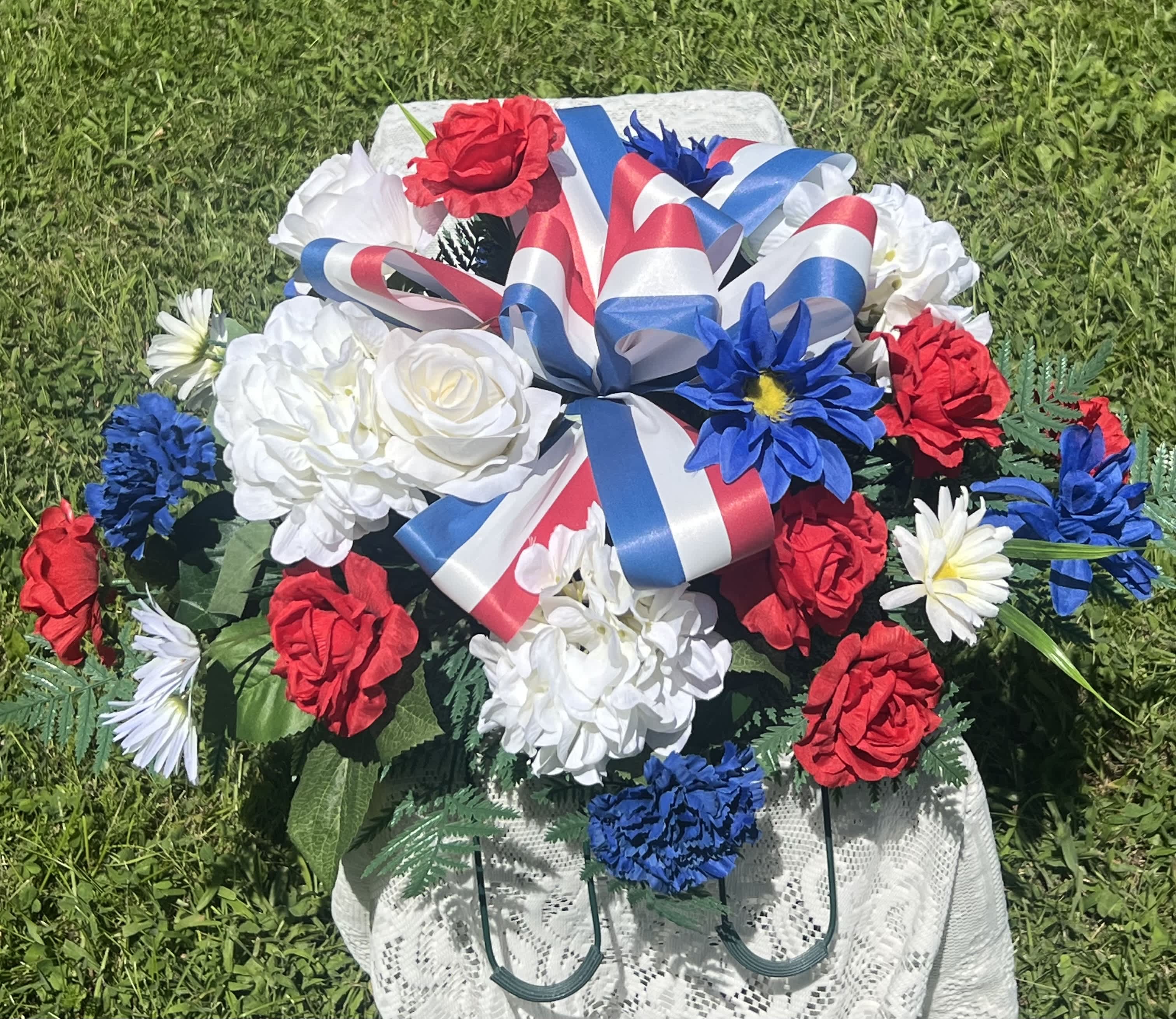 Red, white, and blue floral arrangement with ribbon on a lace-covered stand