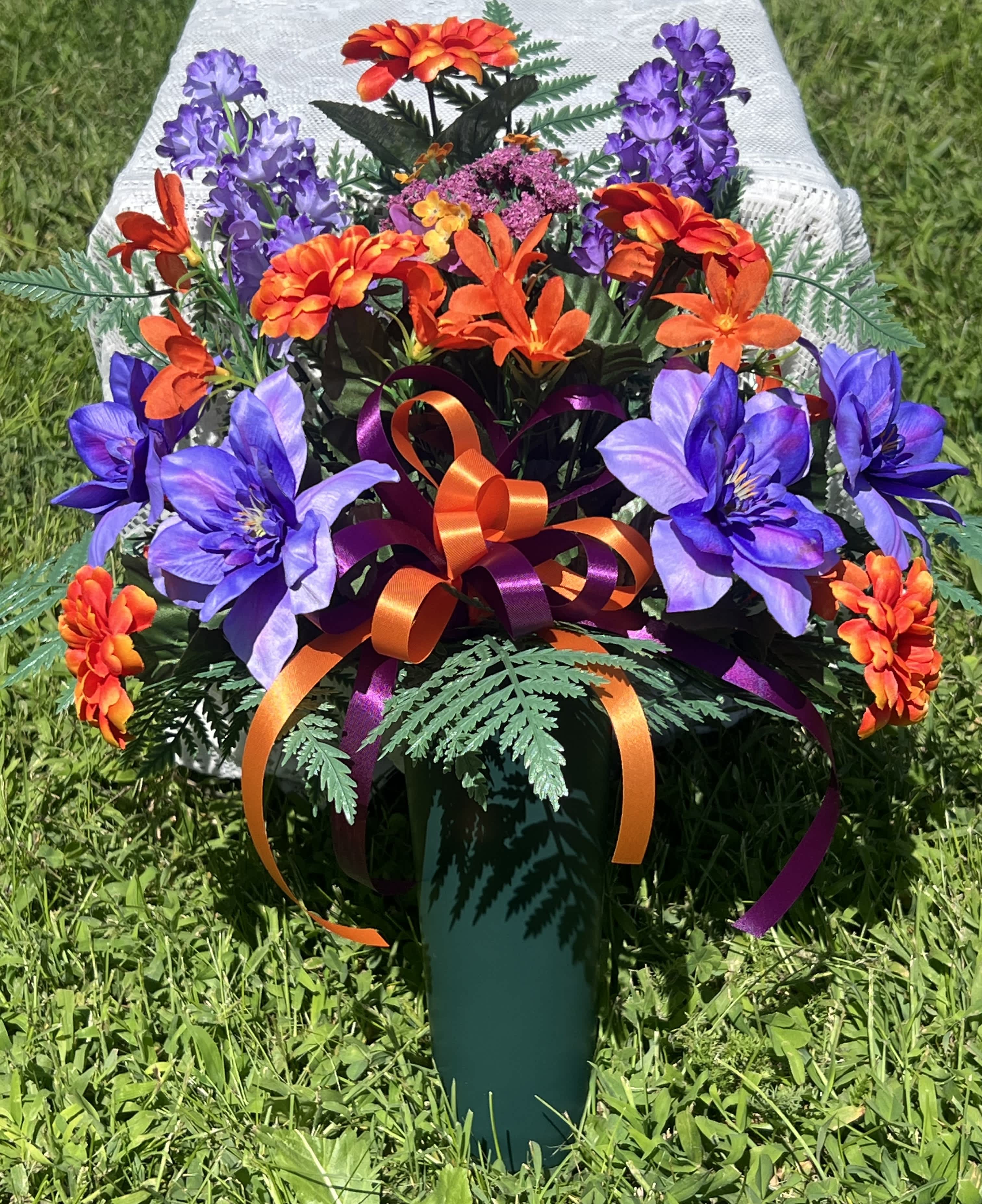 Artificial bouquet of purple and orange flowers in a green vase with ribbon