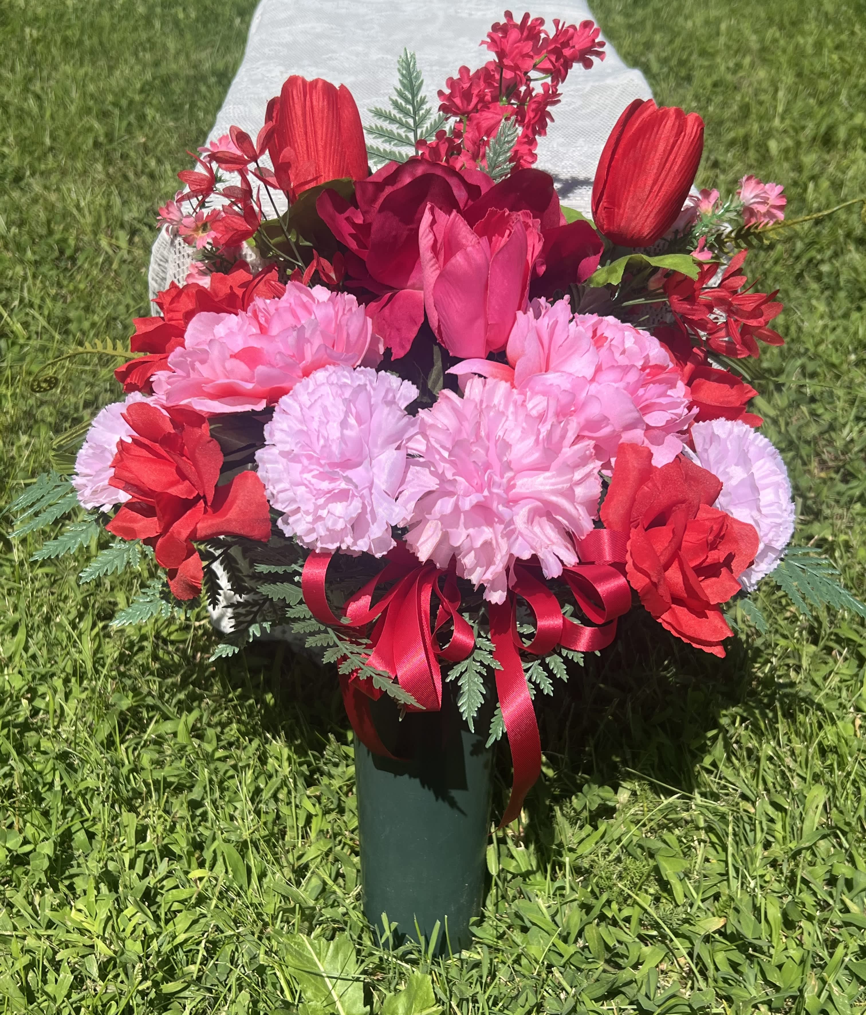 Pink and red floral arrangement in a green vase with a ribbon bow