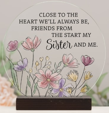 Round memorial plaque with floral illustration and sister quote on a wooden stand