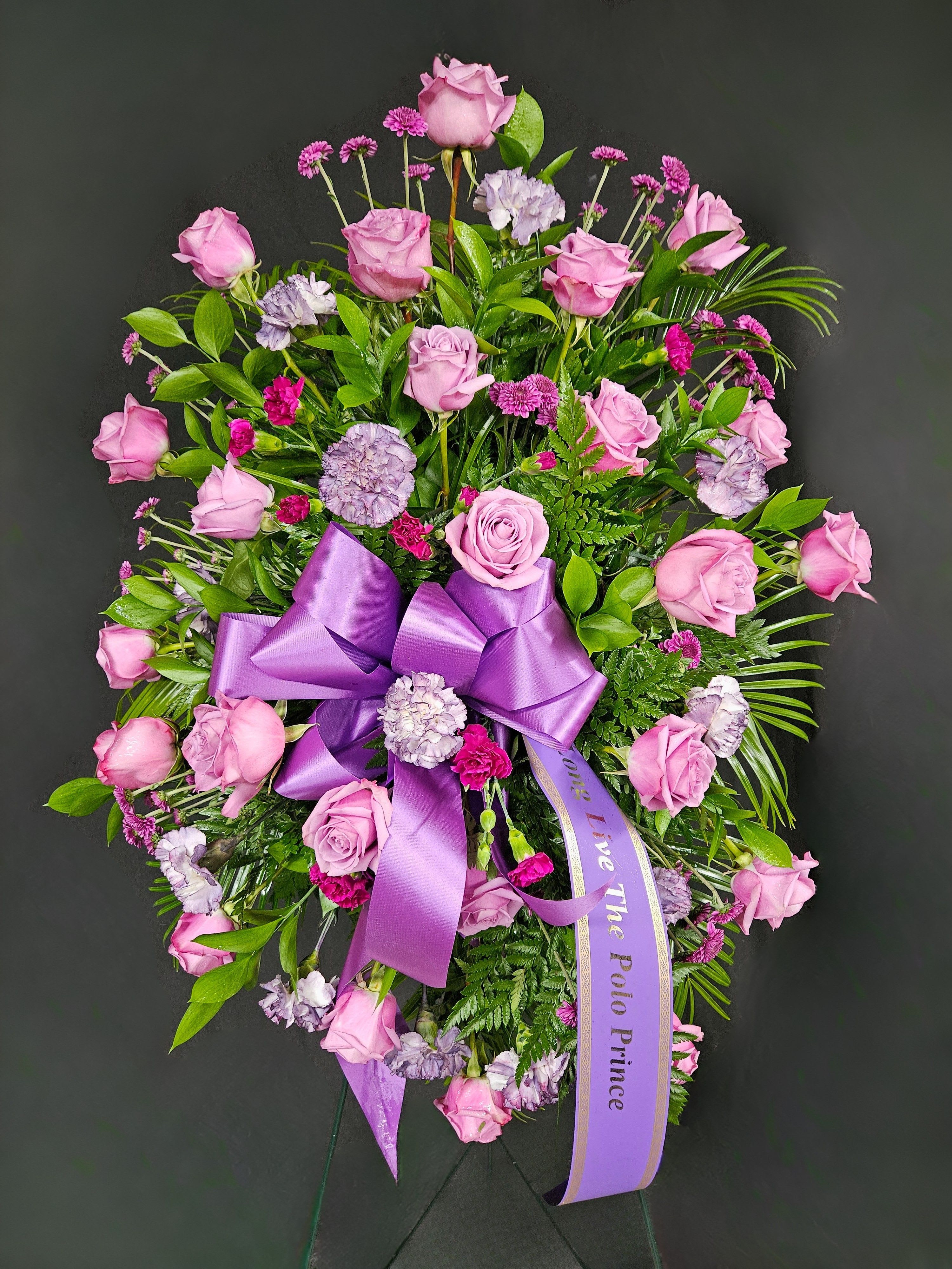 Pink rose and carnation funeral spray with a purple ribbon
