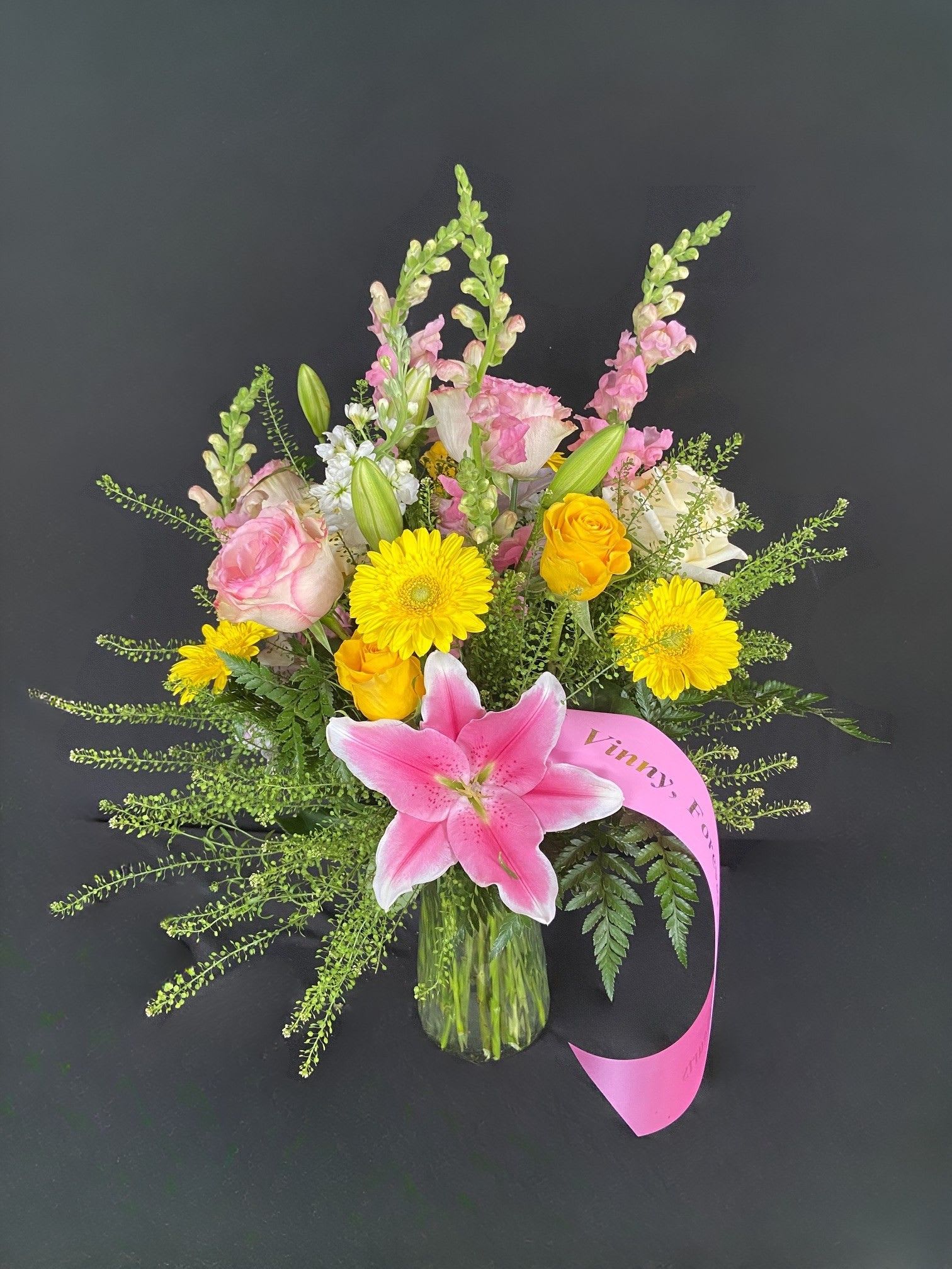 Pink lily bouquet with yellow daisies and roses in a glass vase