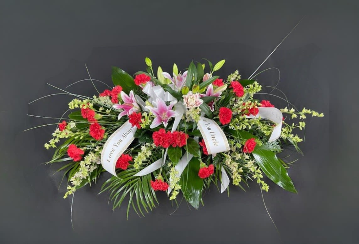 Sympathy spray with pink lilies, red carnations, and white ribbons