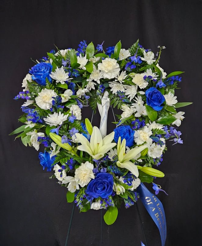Angelic Skies Open Heart Wreath - Although your loved one has passed on, rejoice, for they soar through the heavens on the wings of an Angel. Celebrate their life and honor their memory with this 18" open heart wreath mounted on a 54" standing easel. Arrangement includes a keepsake ceramic Angel displayed among assorted blue and white flowers including roses, lilies, delphinium, carnations, daisies, alstro, and statice. Available in 18" (standard) and 24" (deluxe) sizes.