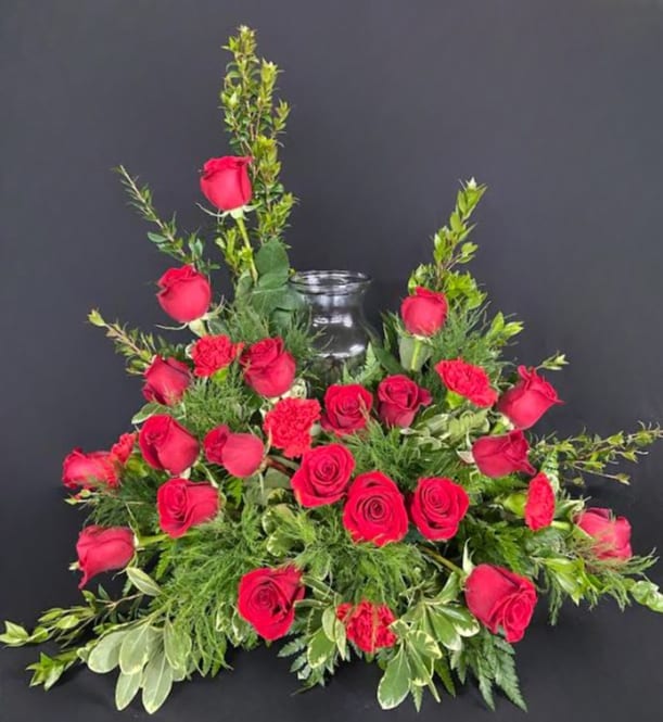Red roses arranged around a clear glass vase with greenery
