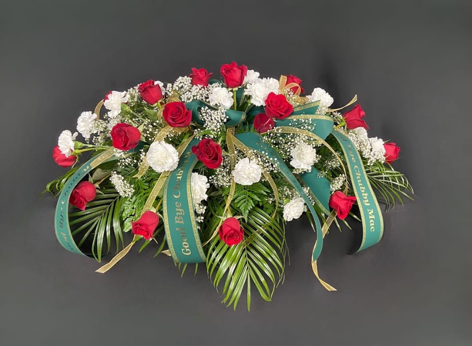 Rosy Day Casket Spray - Two dozen red roses and two dozen white carnations are mingled with sprigs of baby's breath and elegant greens to make this casket spray. Upgrade to deluxe to add an additional 6 roses and 6 carnations. Upgrade to premium to add an additional 12 roses and 12 carnations. Price includes up to 4 custom printed ribbons.