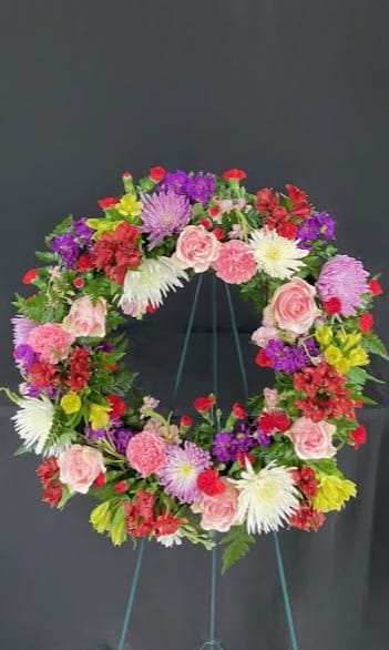 Colorful floral wreath on a stand with pink, red, purple, and white blooms