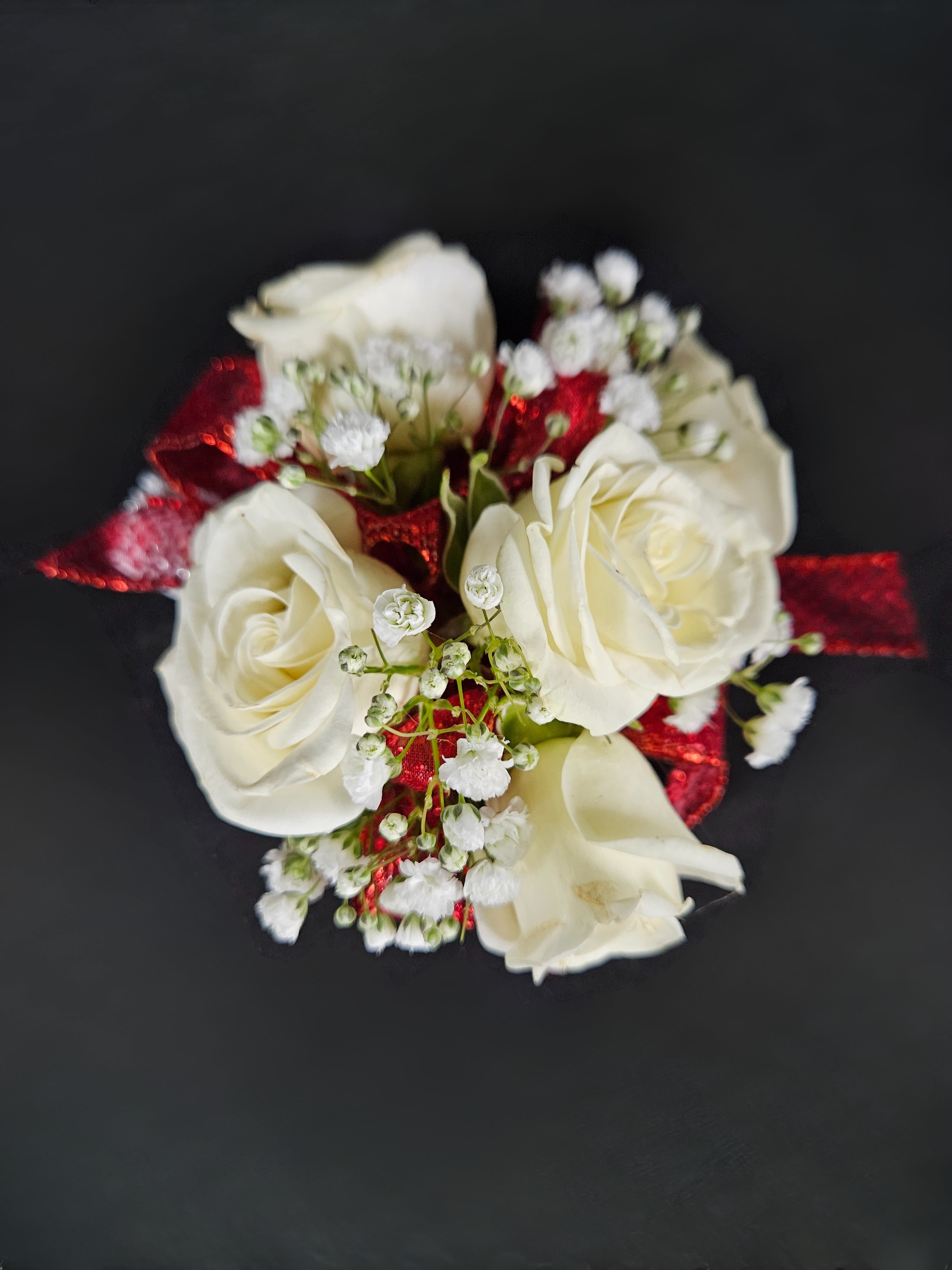 Small cluster of white roses with baby's breath and red ribbon on a dark background