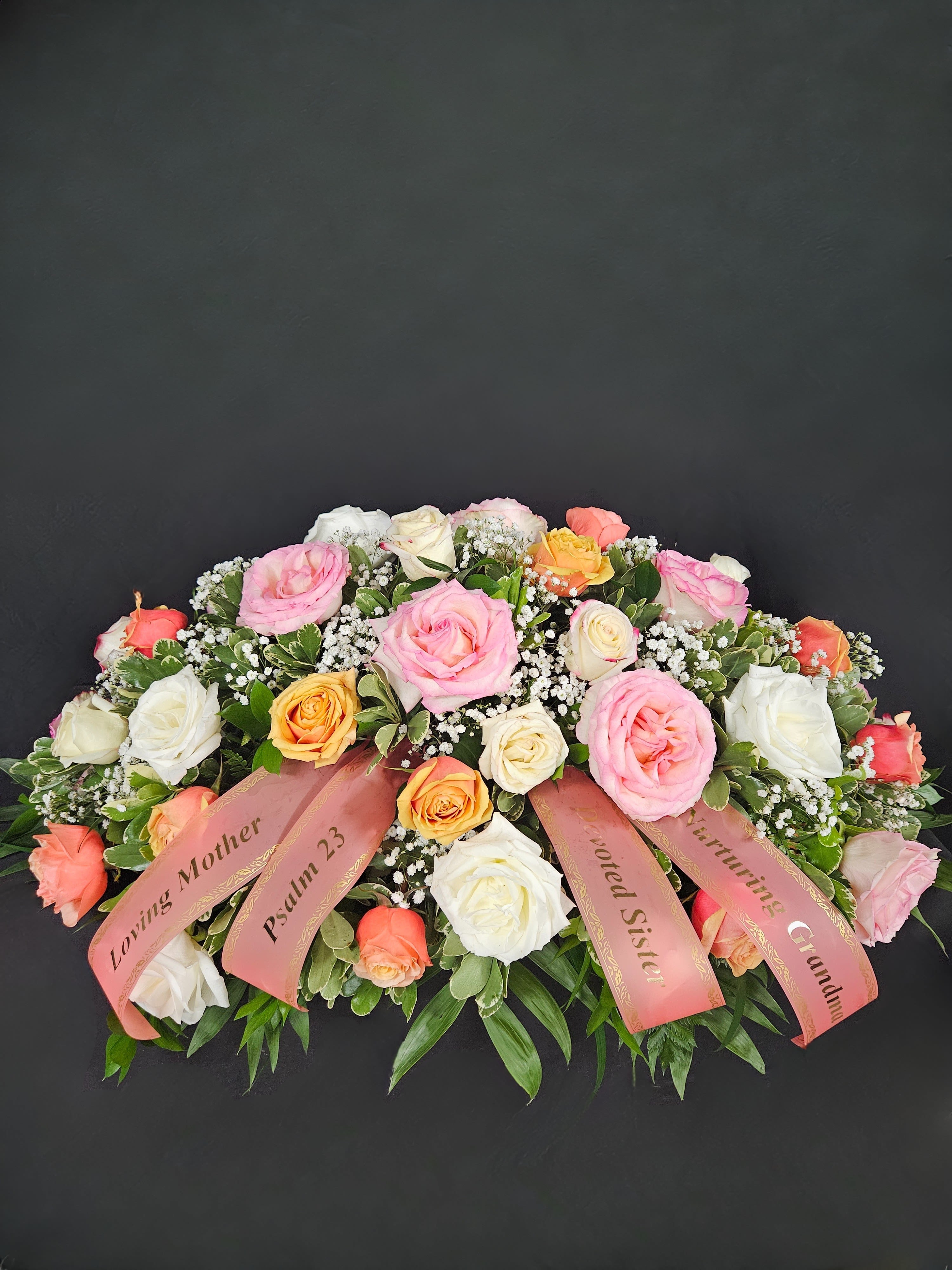 Large pink, white, and peach rose arrangement with ribbons on a dark background