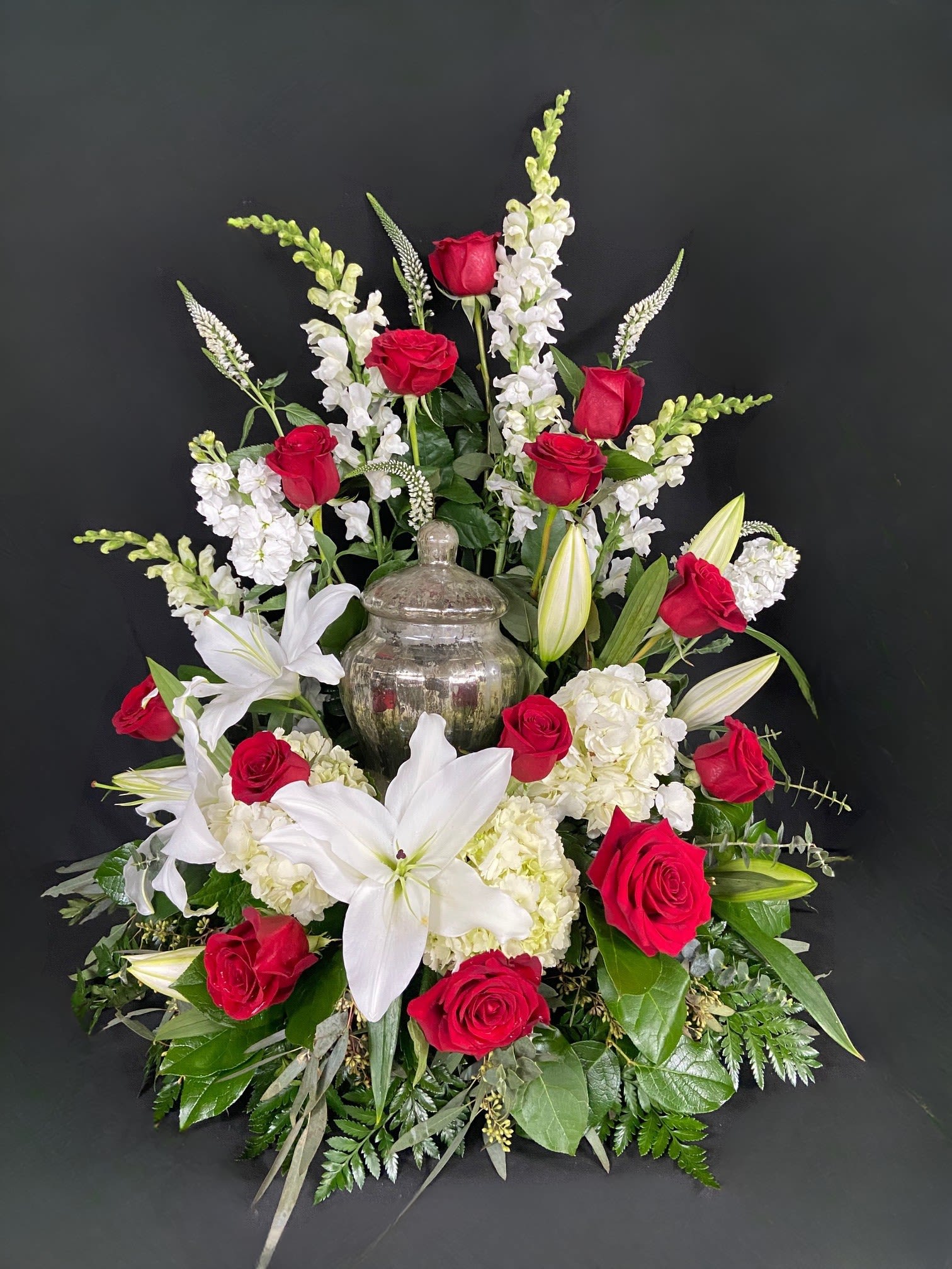 Missing You Urn Design - Honor and celebrate the fruitful life of a lost loved one with an arrangement that truly encompasses their elegance. The Missing You Urn arrangement is a luxurious addition to any memorial service. This arrangement features majestic white hydrangeas that will ease the minds and comfort the souls that are grieving with contrasting red roses to represent the vibrance of their life