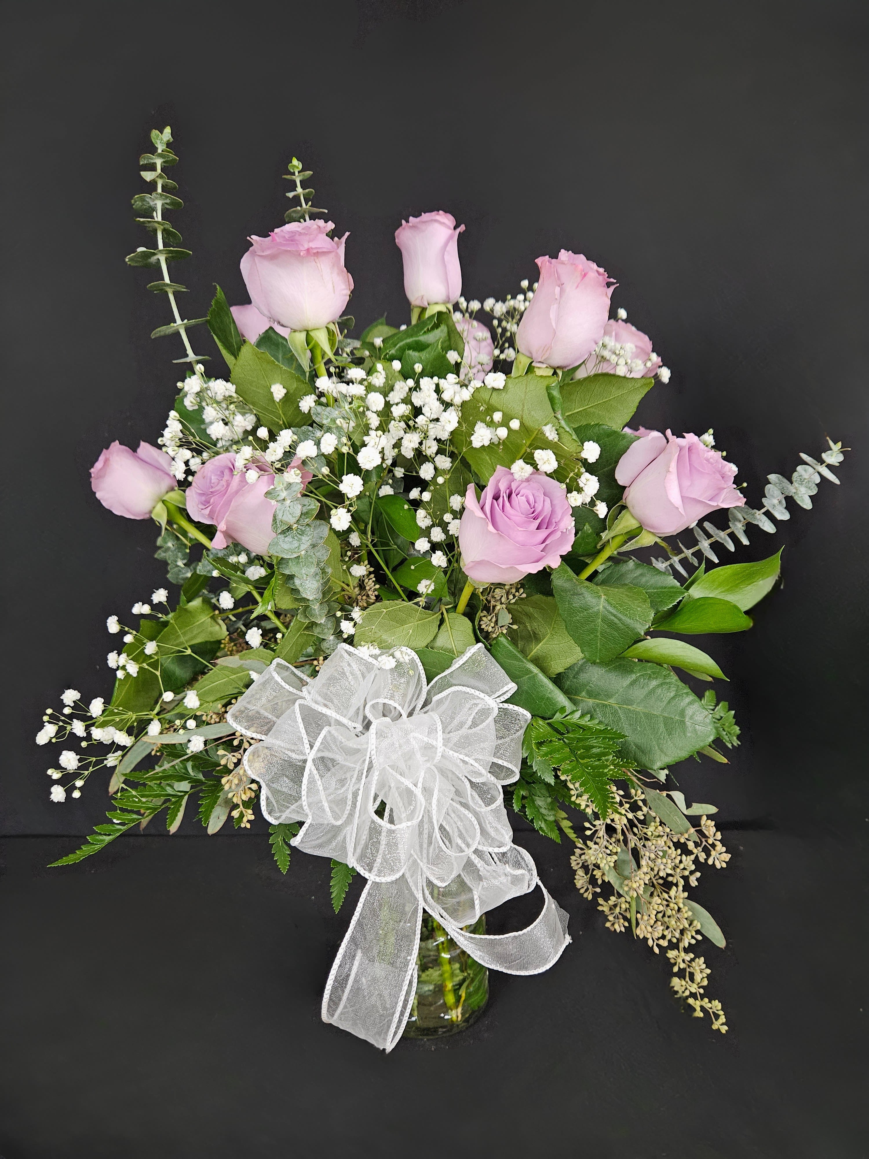 Pink roses and baby's breath in a glass vase with a white bow